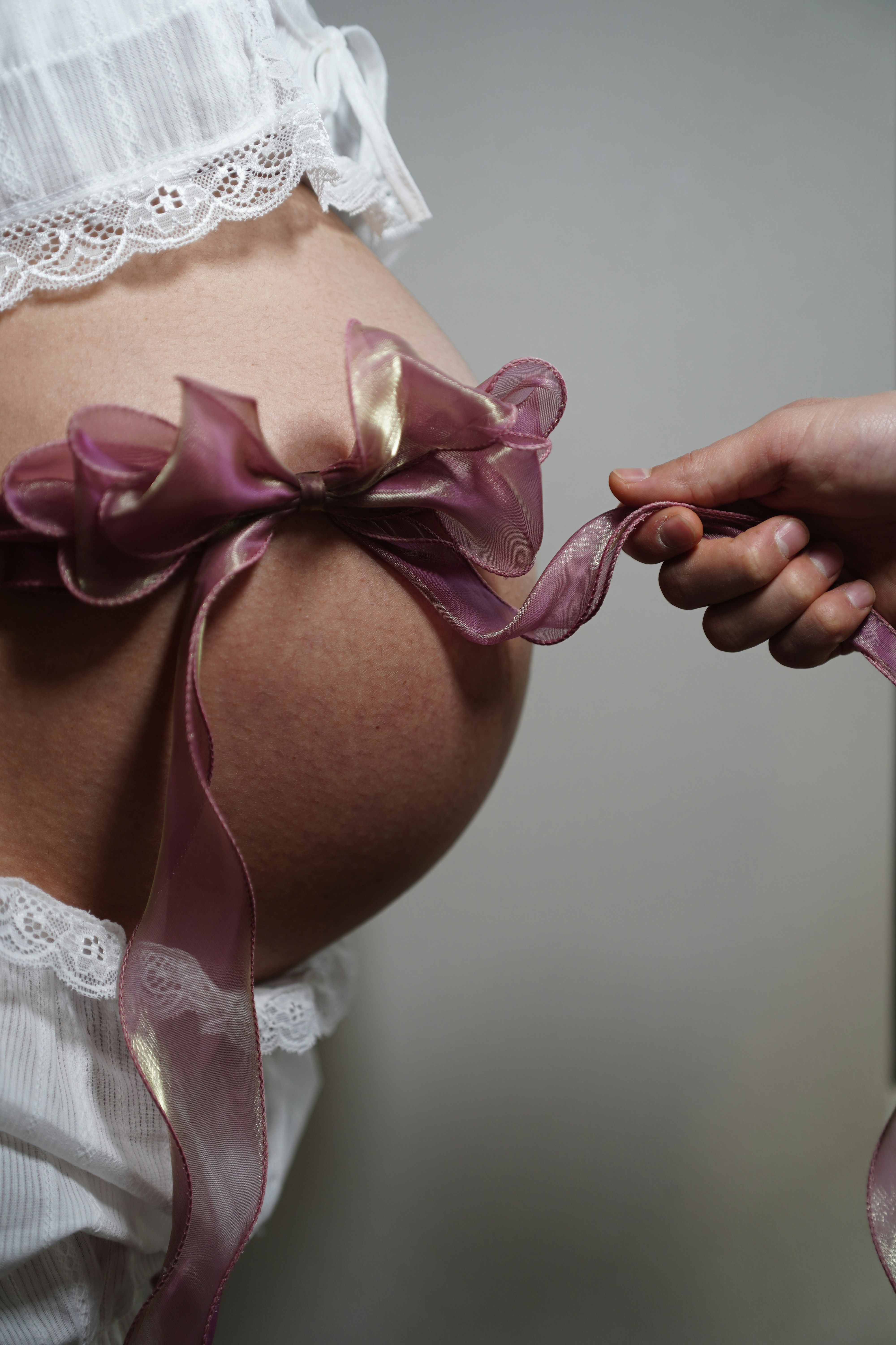 A hand ties a ribbon around a pregnant belly.