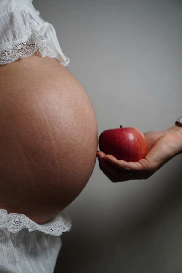 Vientre de embarazo con mano ofreciendo manzana, nutrición materno-infantil