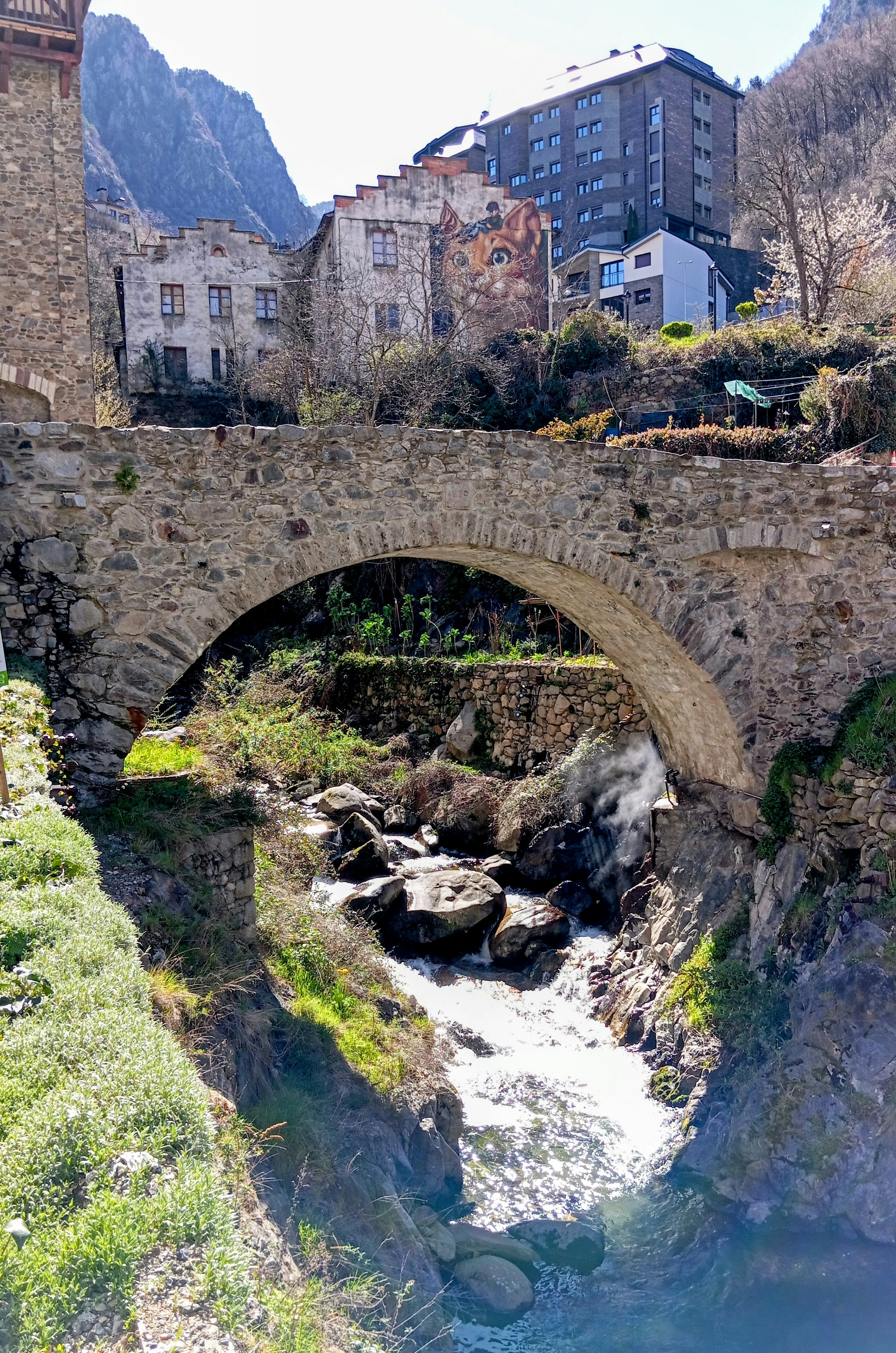 Stone bridge over a rocky stream with buildings above