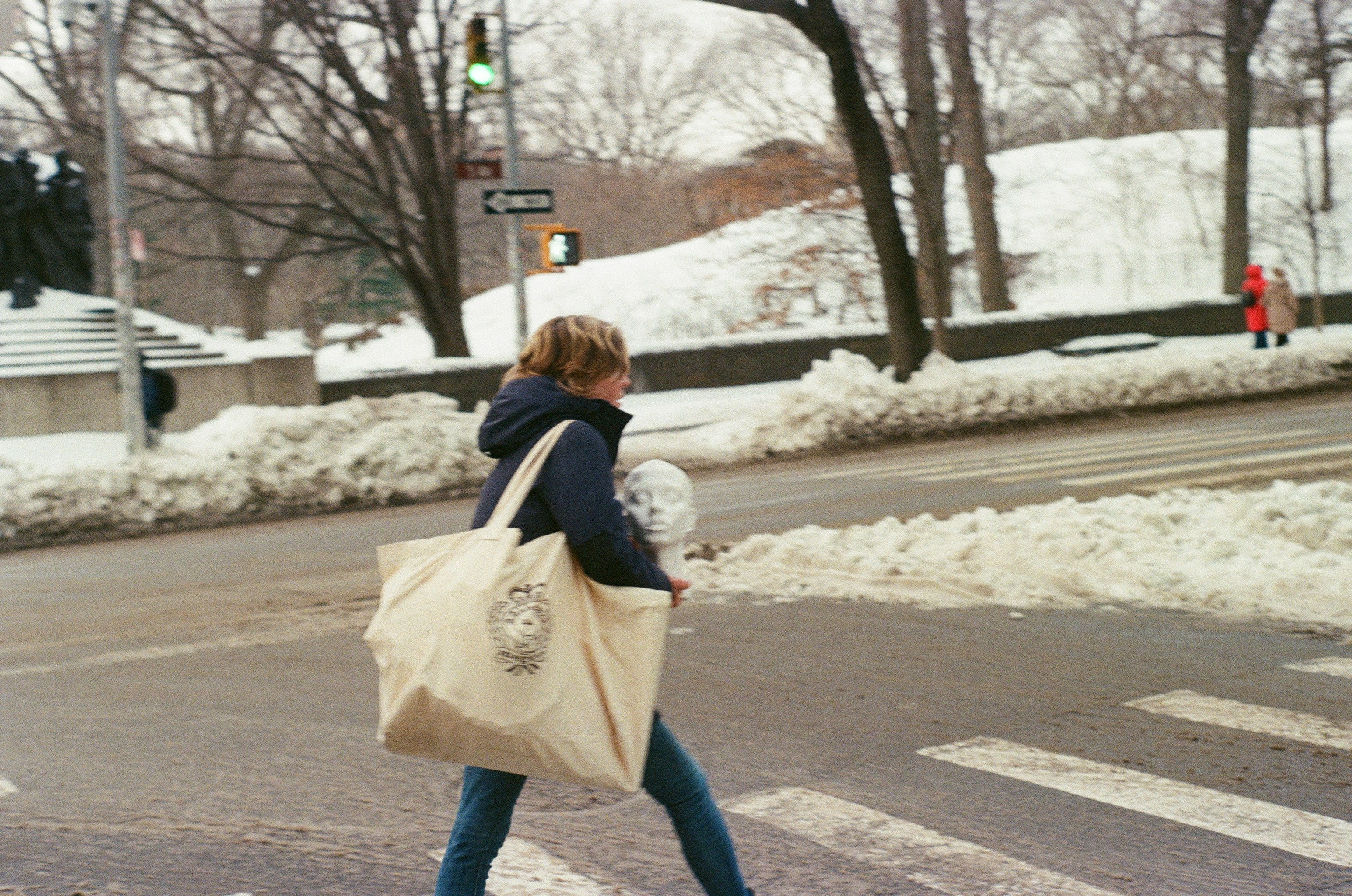 Woman with large tote bag crosses snowy street.