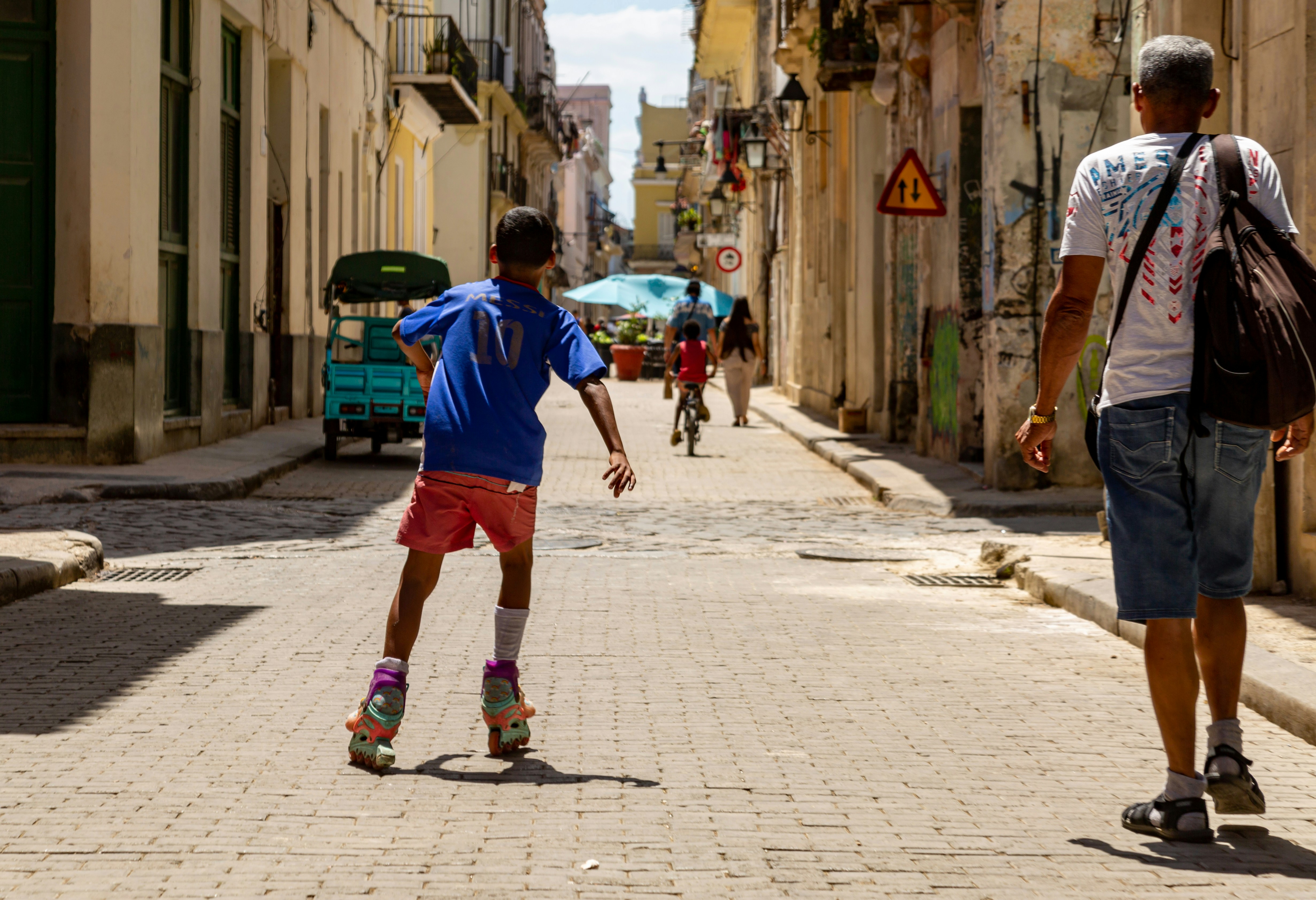 Un garçon fait du roller dans une rue ensoleillée avec des gens.