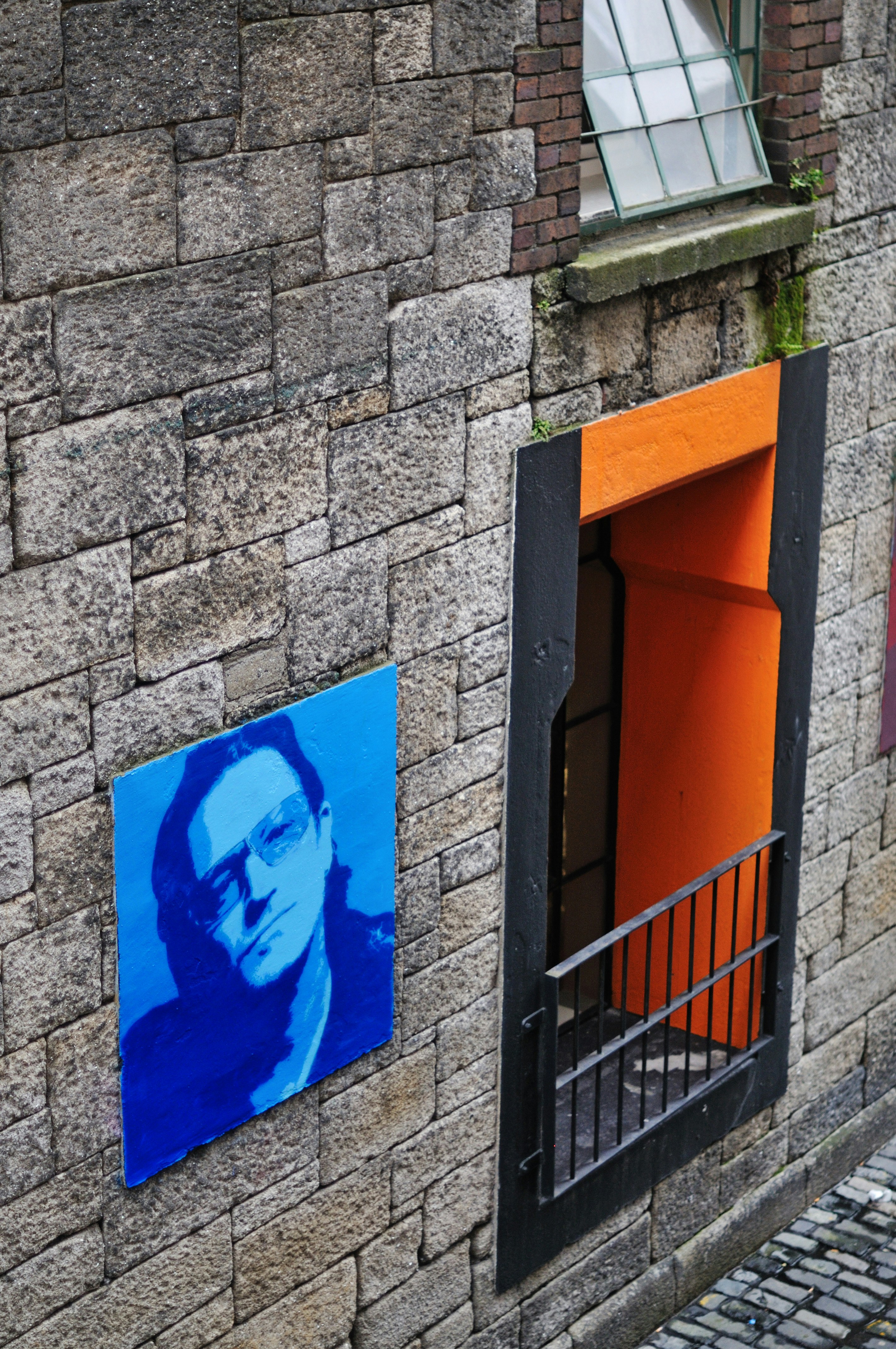 Blaue Porträtkunst an der Steinwand neben der orangefarbenen Tür