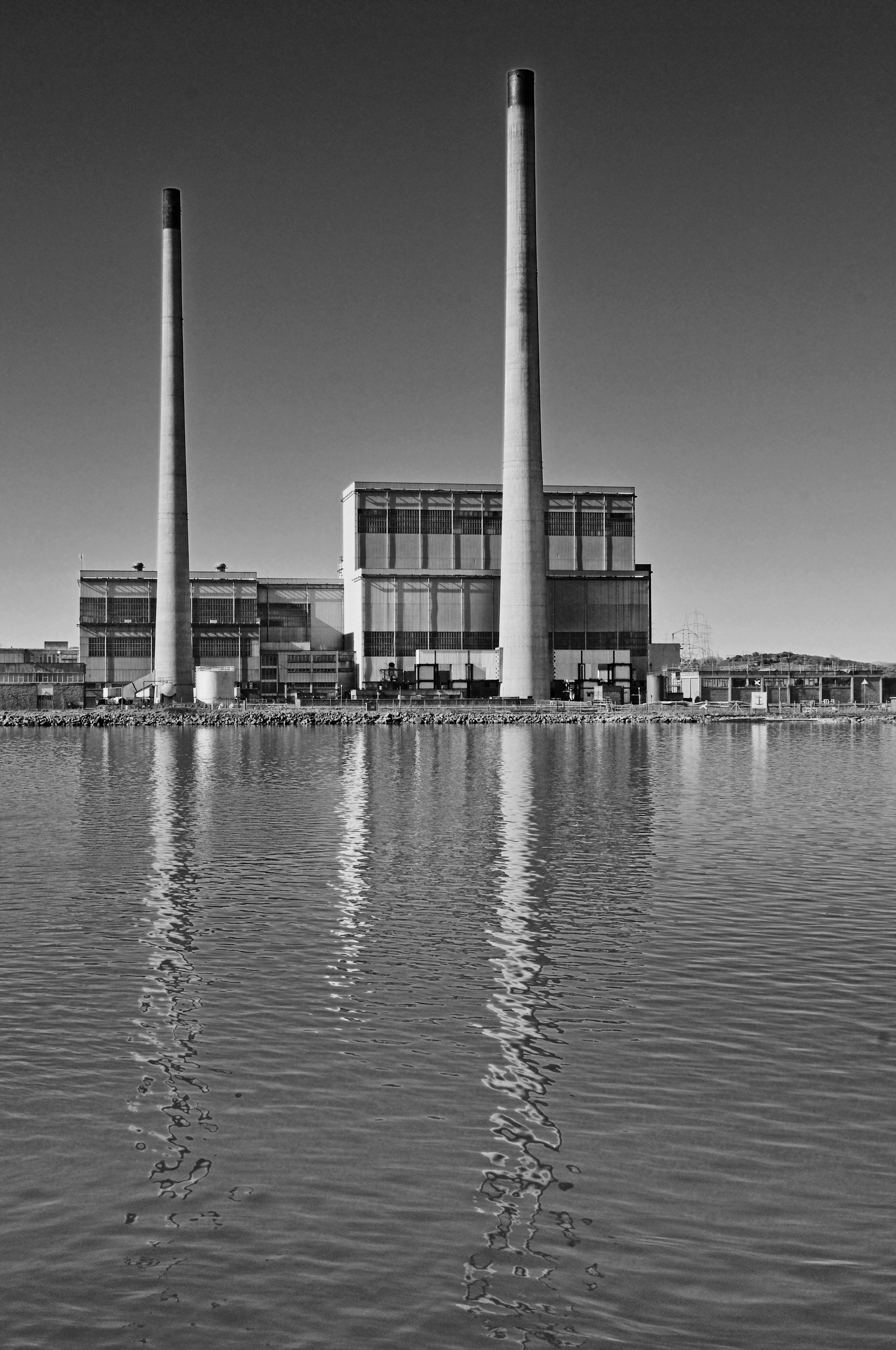 Industriekraftwerk mit hohen Schornsteinen, die sich im Wasser spiegeln