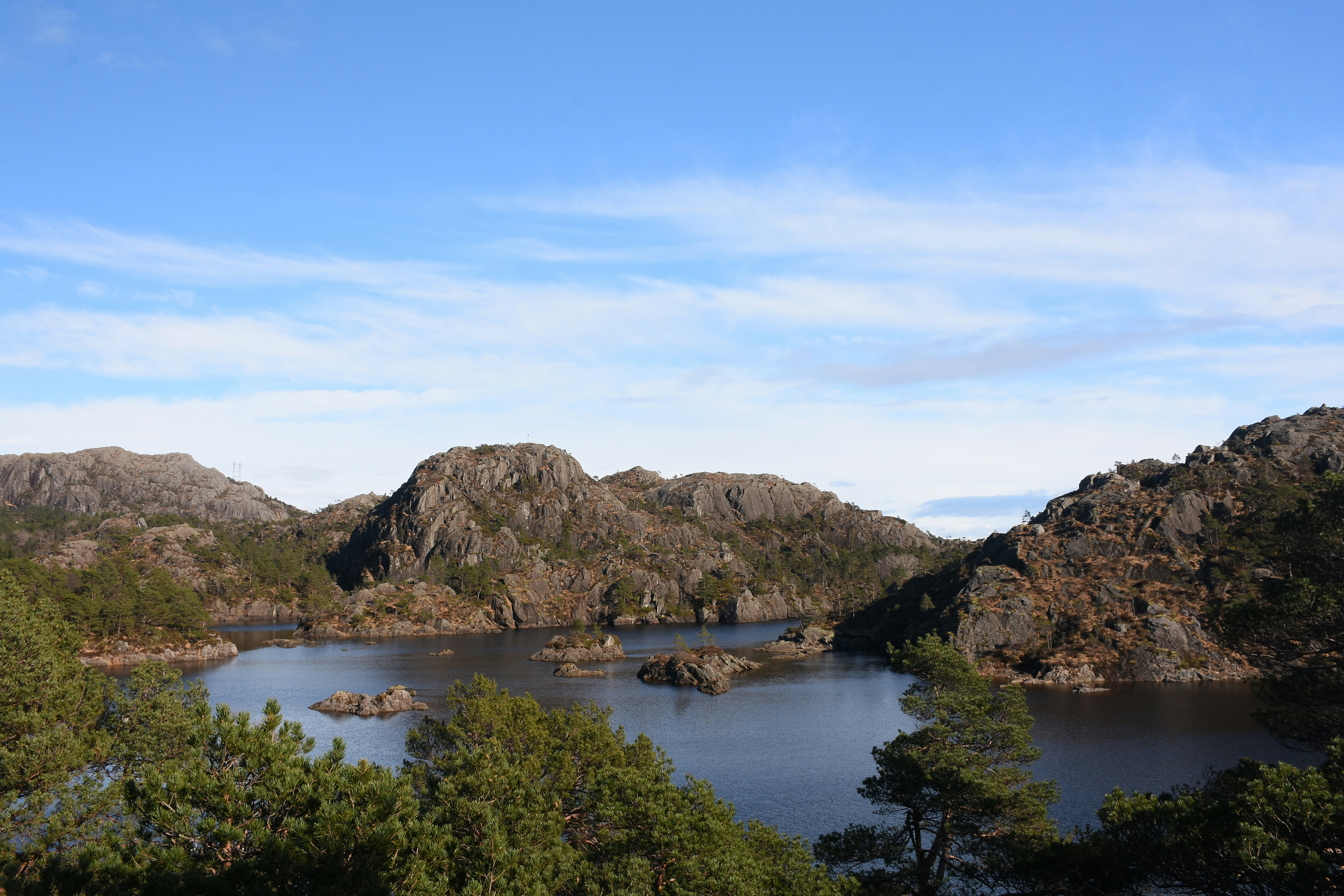Colinas rochosas cercam um lago escuro sob um céu azul.