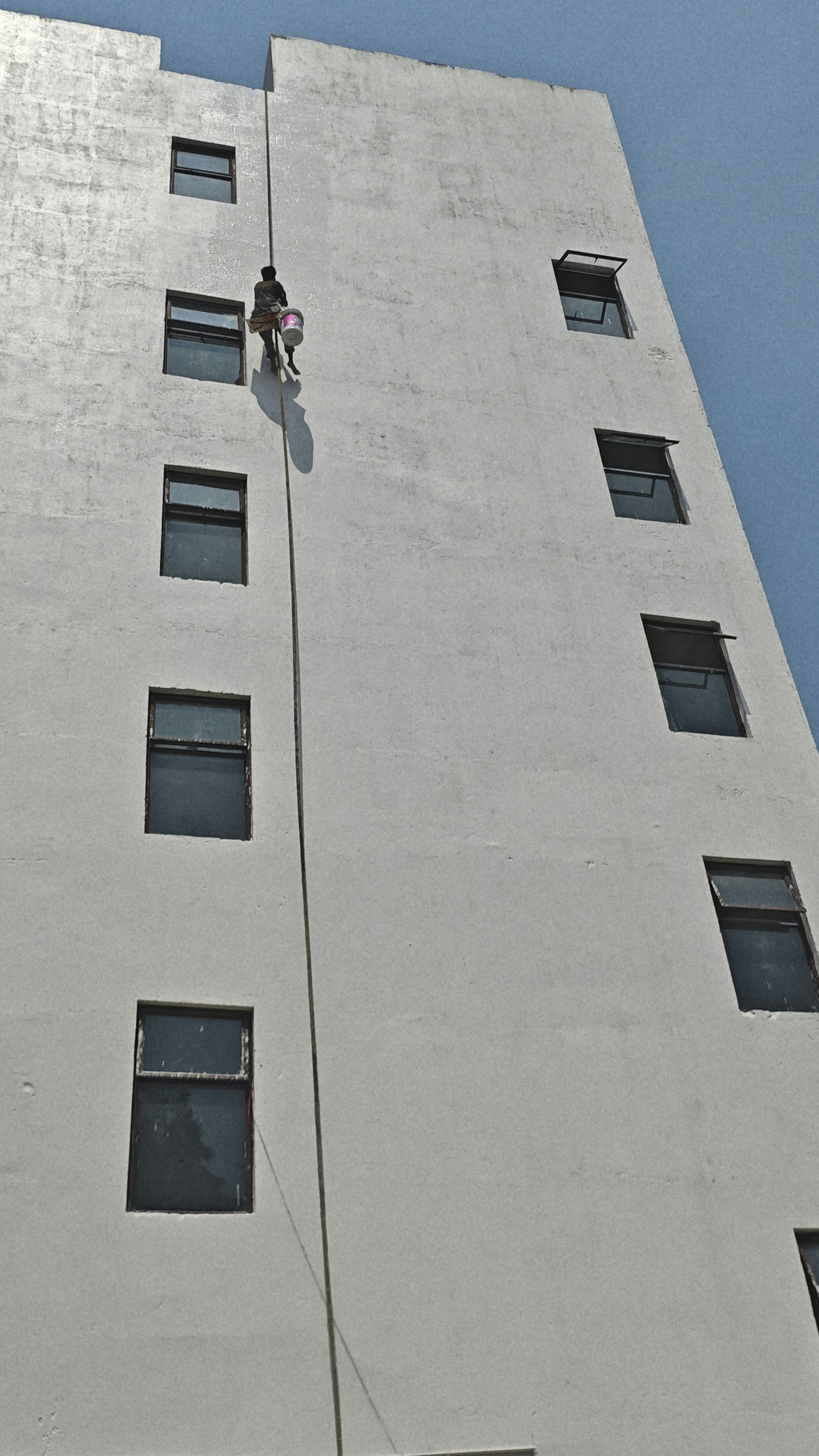 Um trabalhador desce de rapel para lavar as janelas.