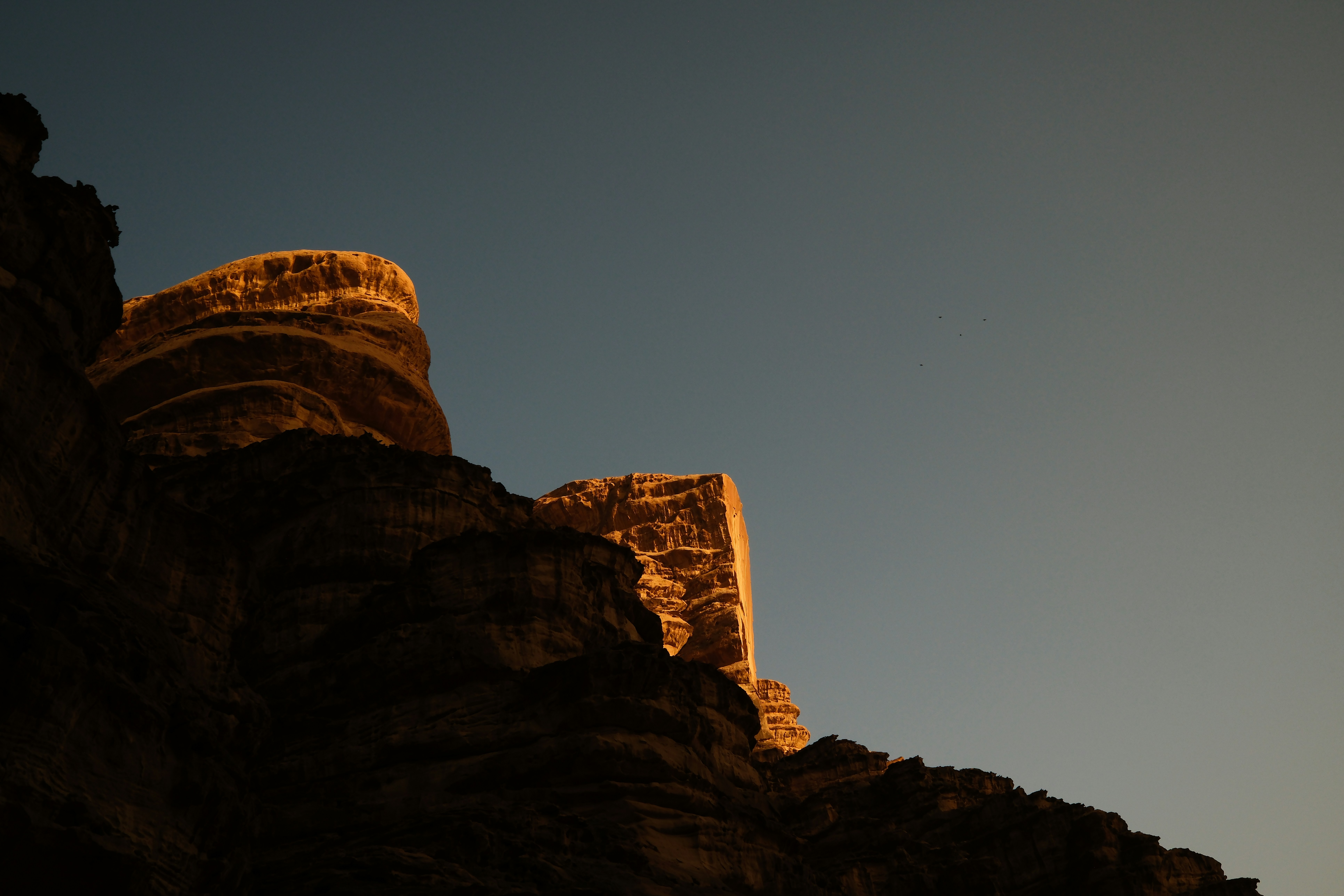 Golden sunlight illuminates rock formations against a clear sky.