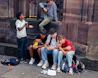 A group of teenagers sitting and standing outside.