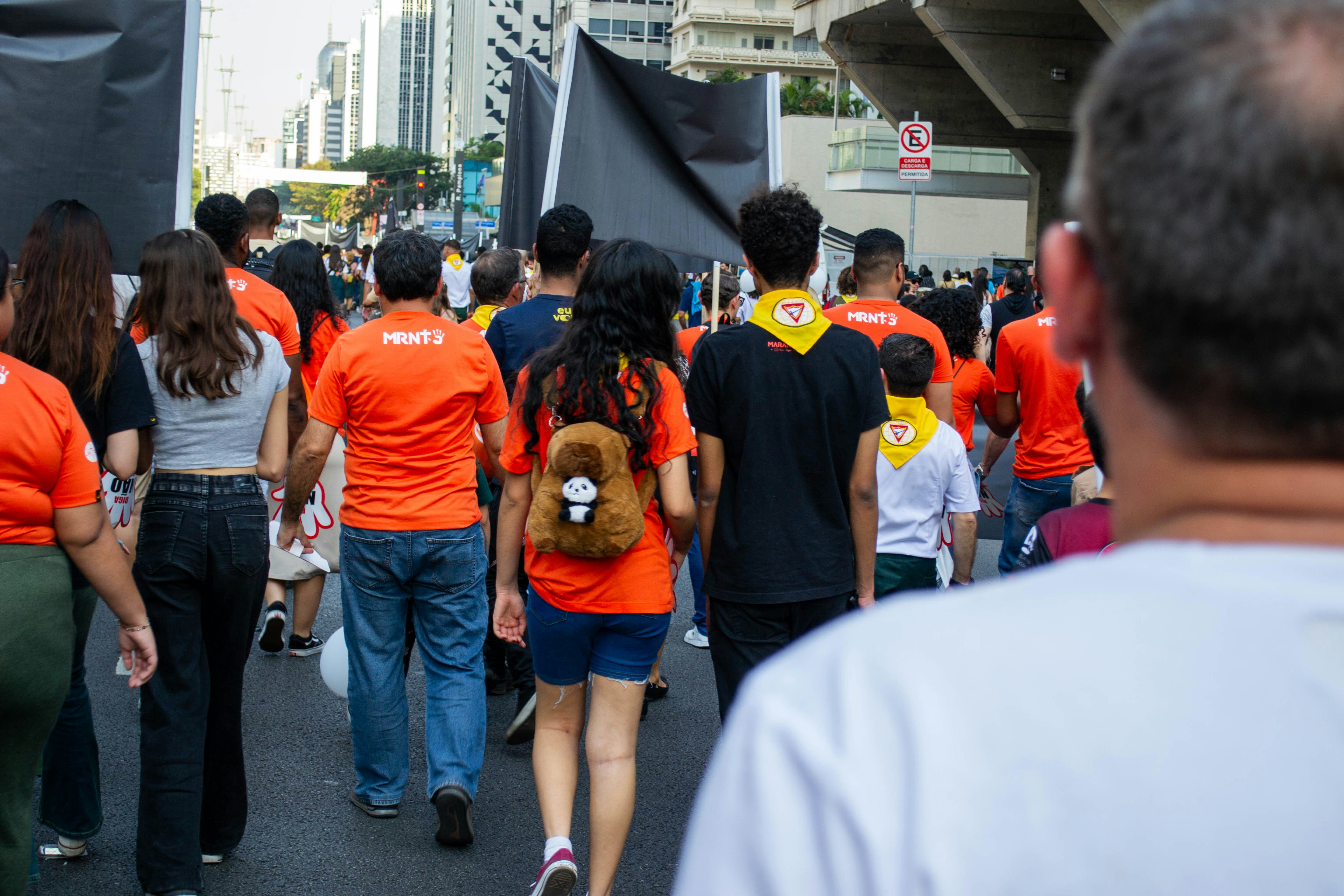 People in orange shirts walking down a city street.
