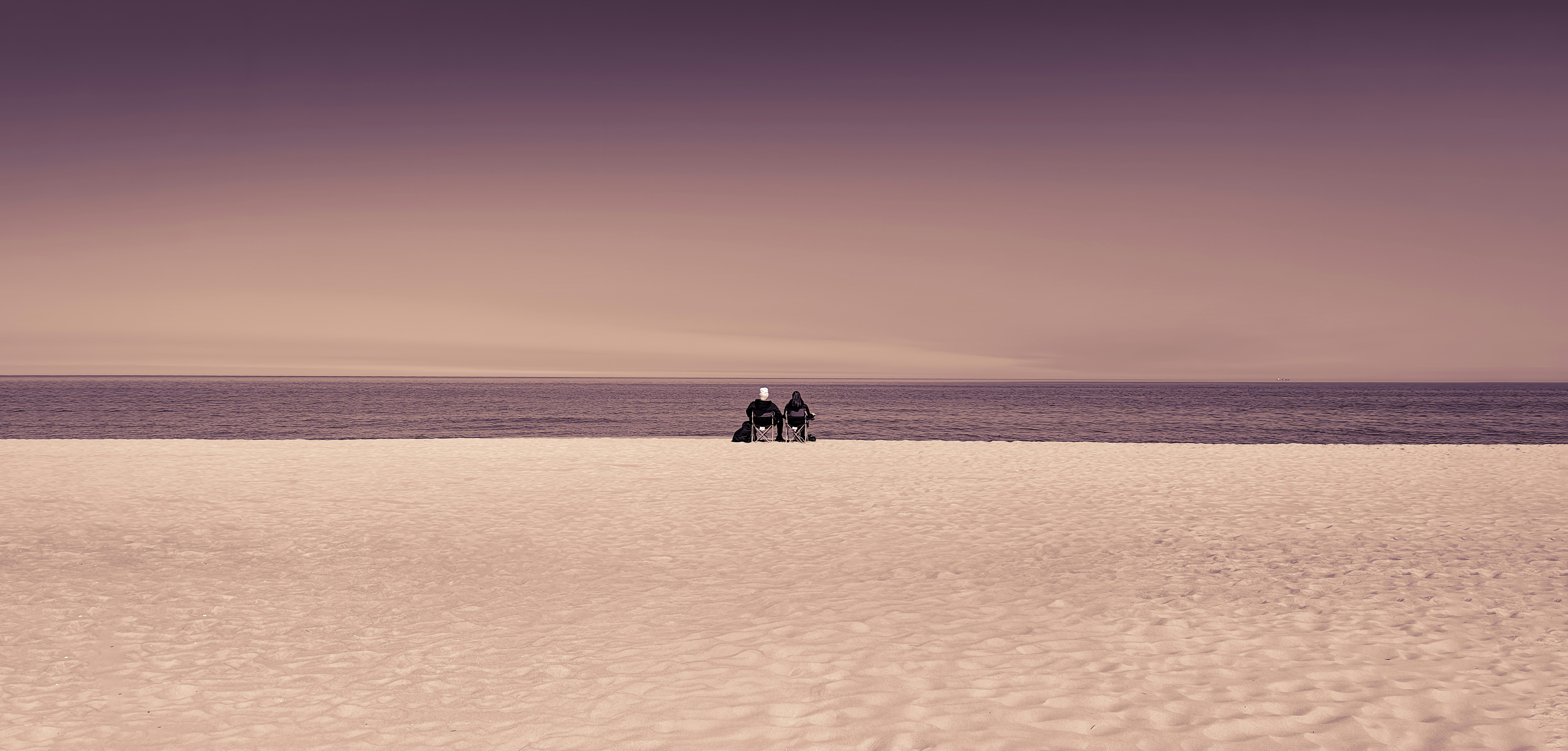 Zwei Menschen sitzen an einem Strand mit Blick auf das Meer