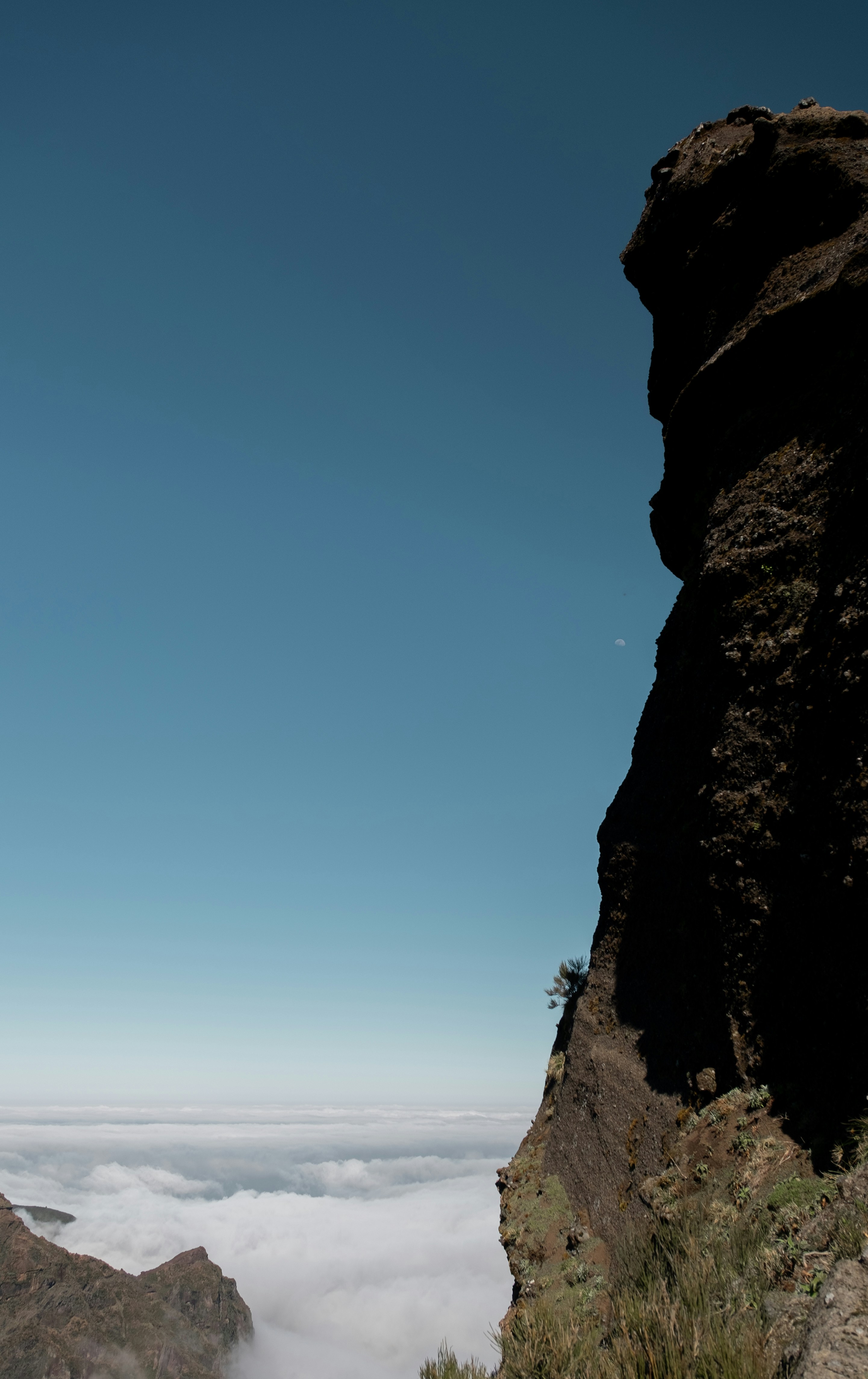 Dramatic cliff face above sea of clouds under blue sky