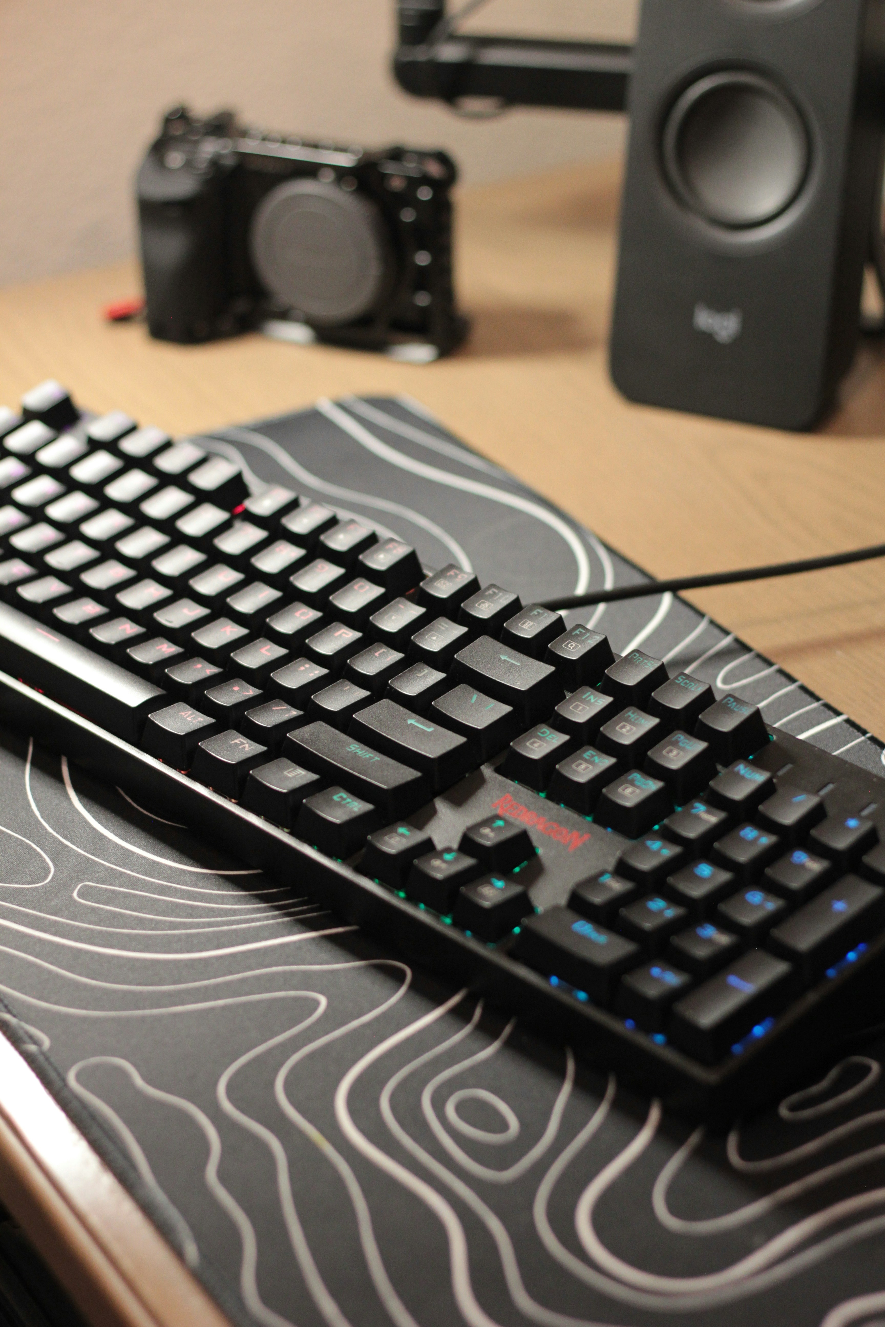 Un teclado mecánico negro sobre un escritorio con cámara.