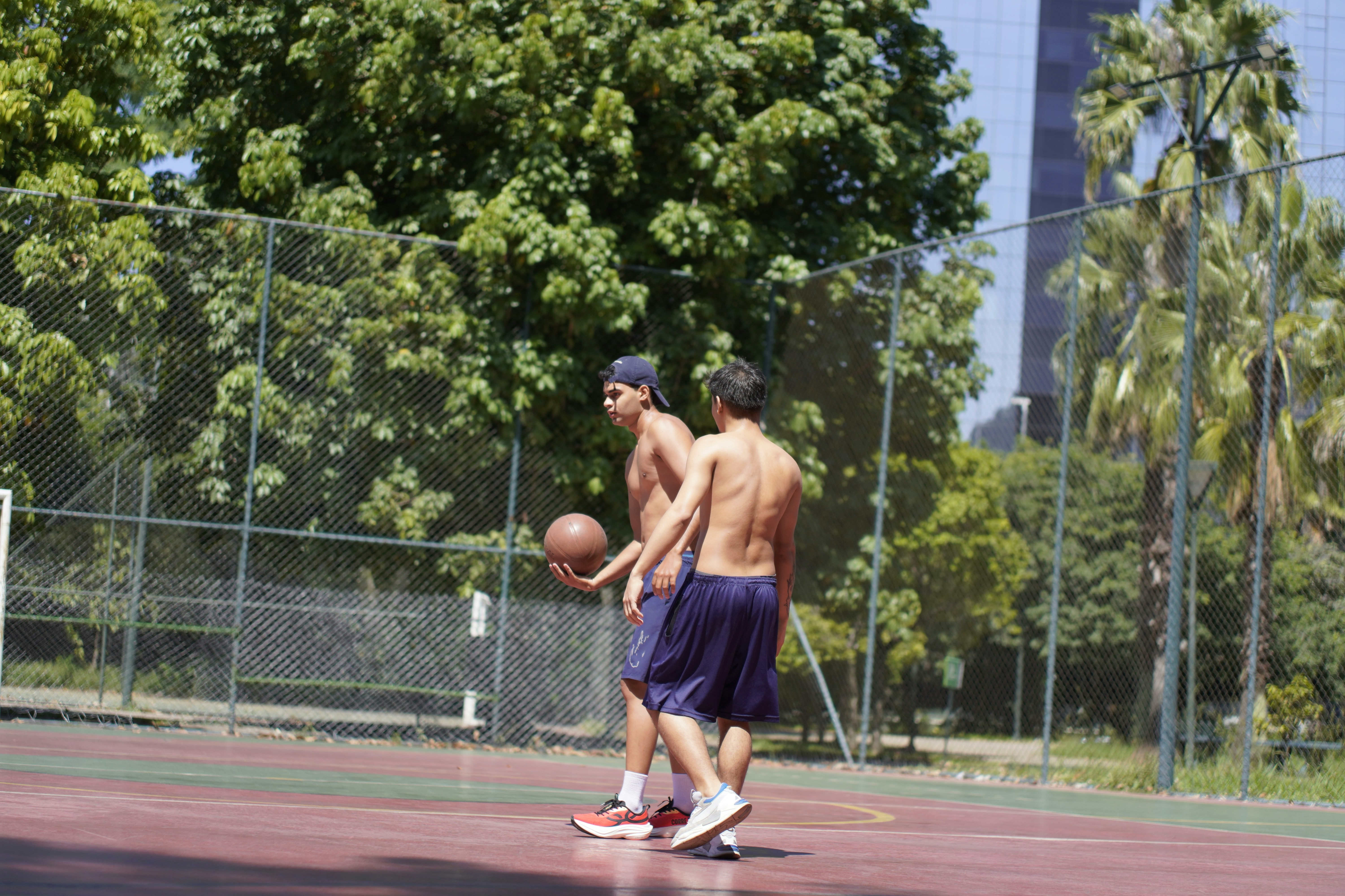 Two shirtless men playing basketball on an outdoor court.