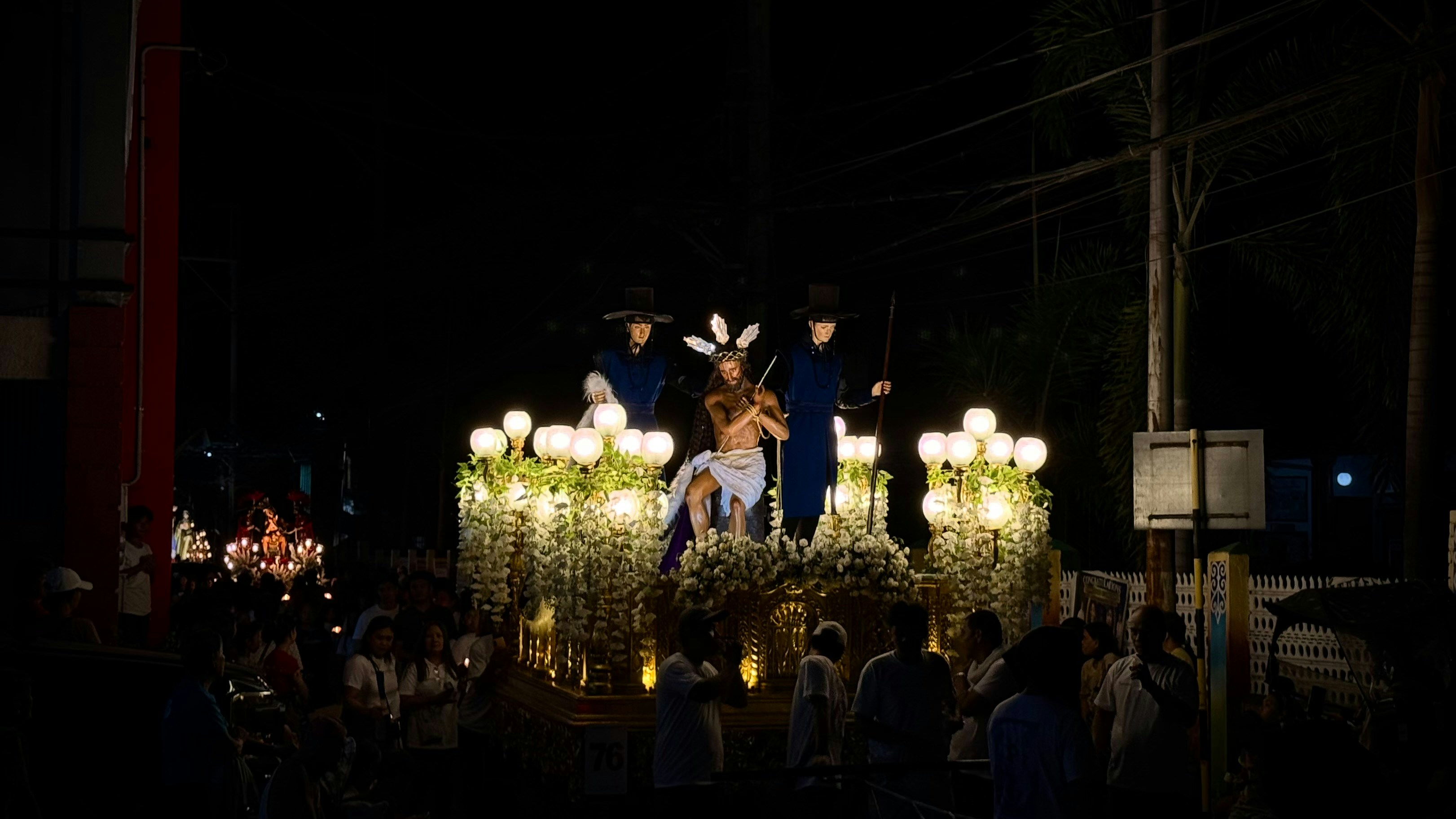 Religious procession at night with illuminated floats and decorated float.
