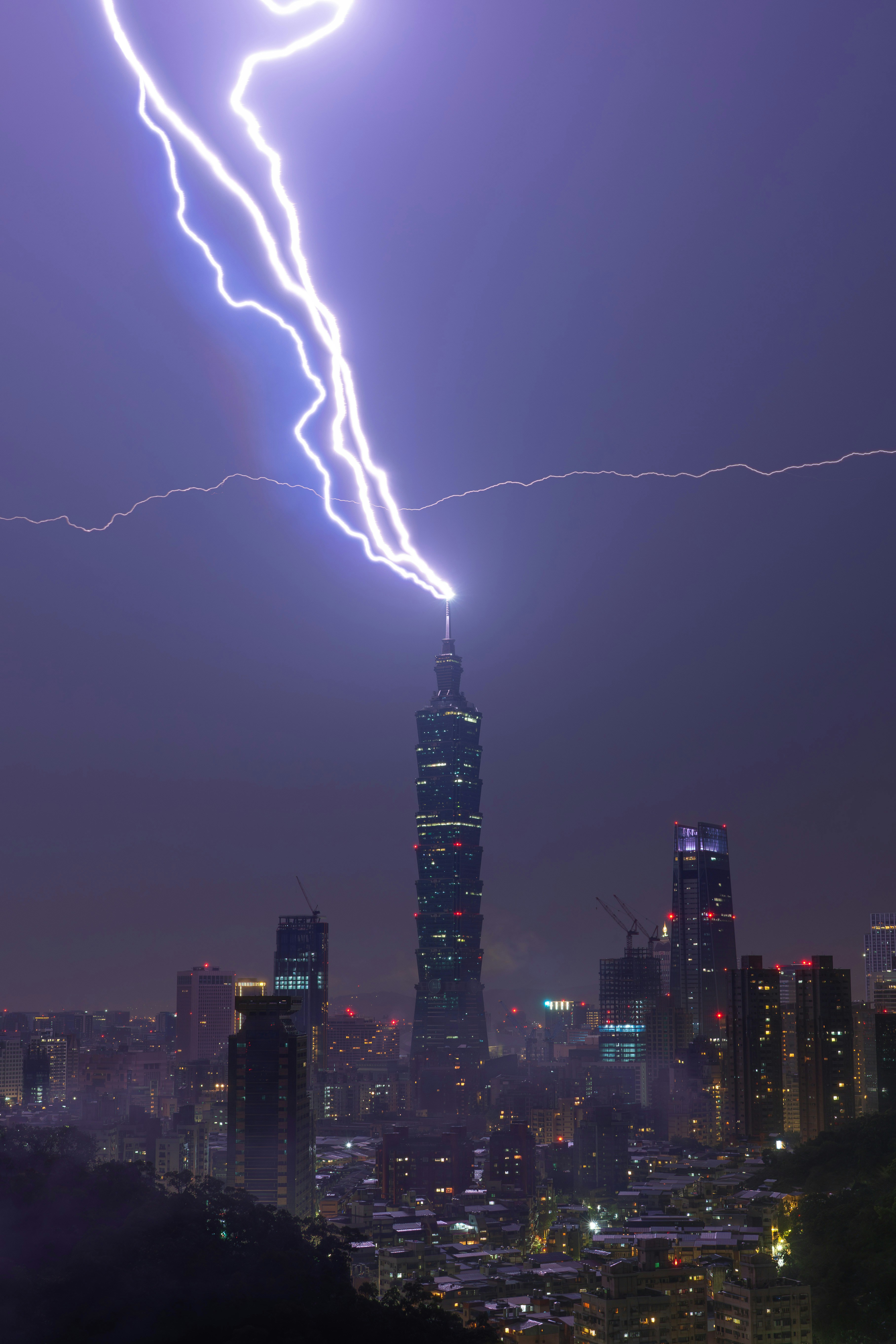 Lightning strikes a tall skyscraper in a city at night.