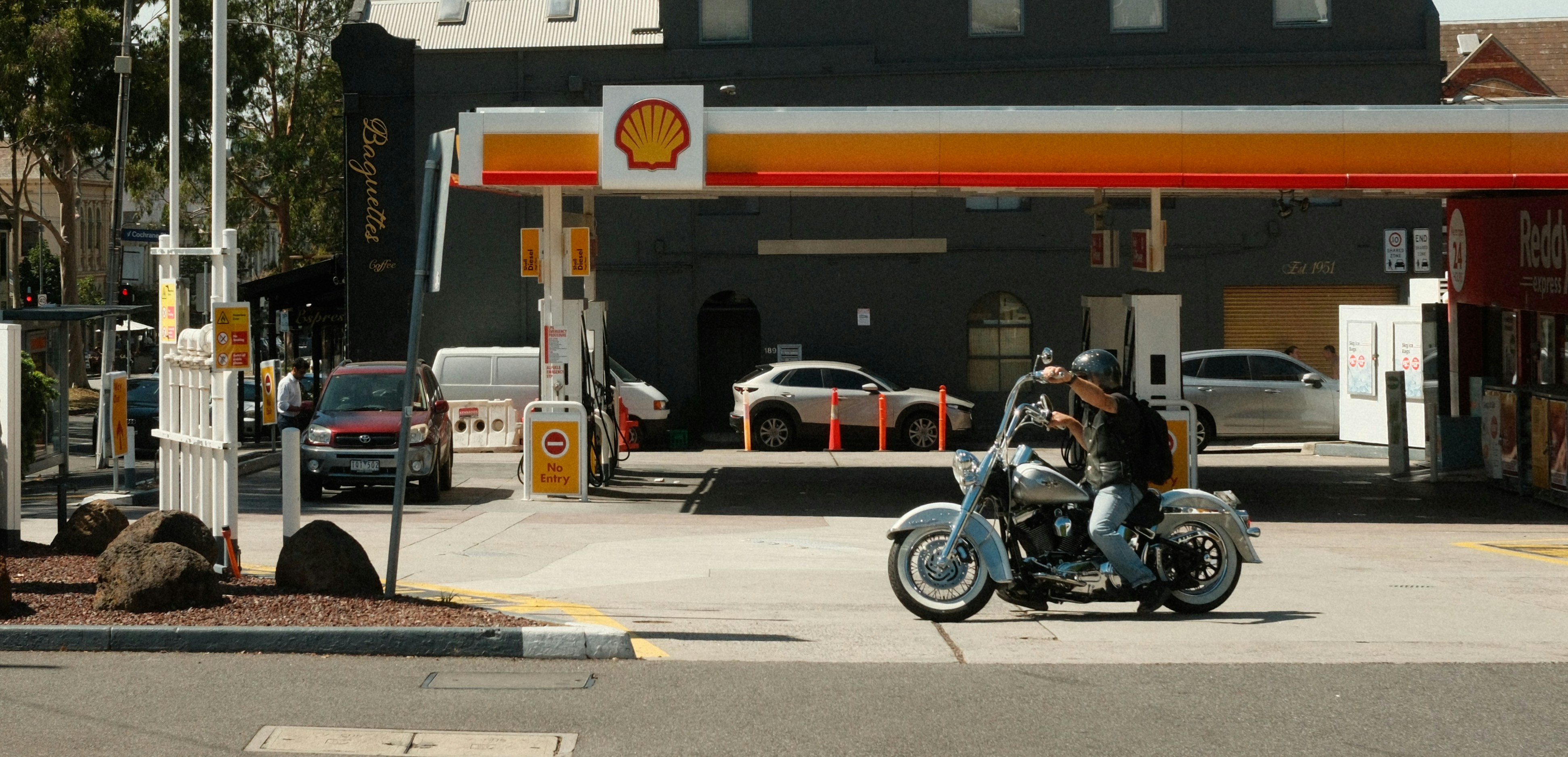 Un homme fait de la moto dans une station-service Shell.