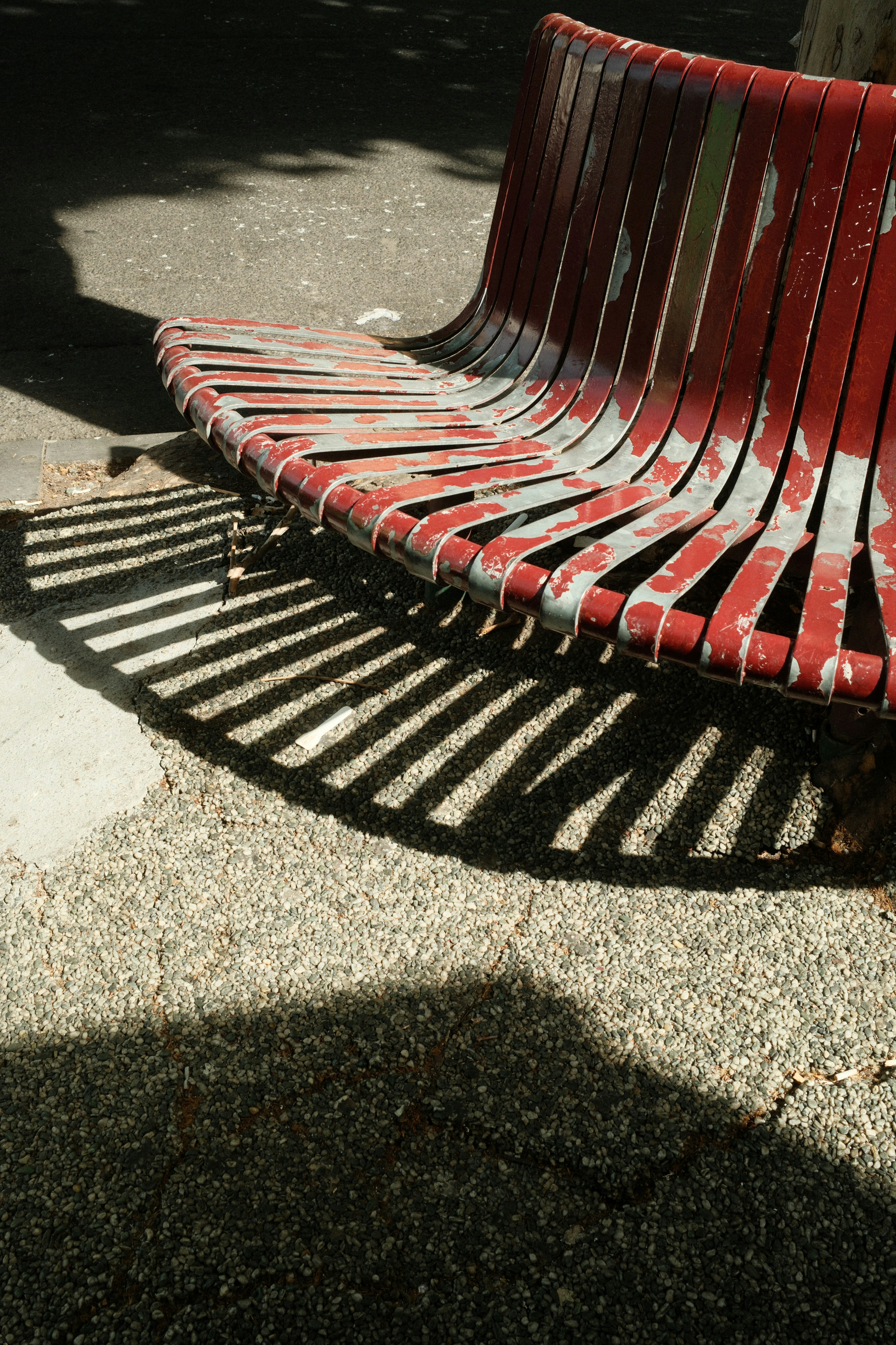 Un banc de parc rouge usé avec des ombres rayées.