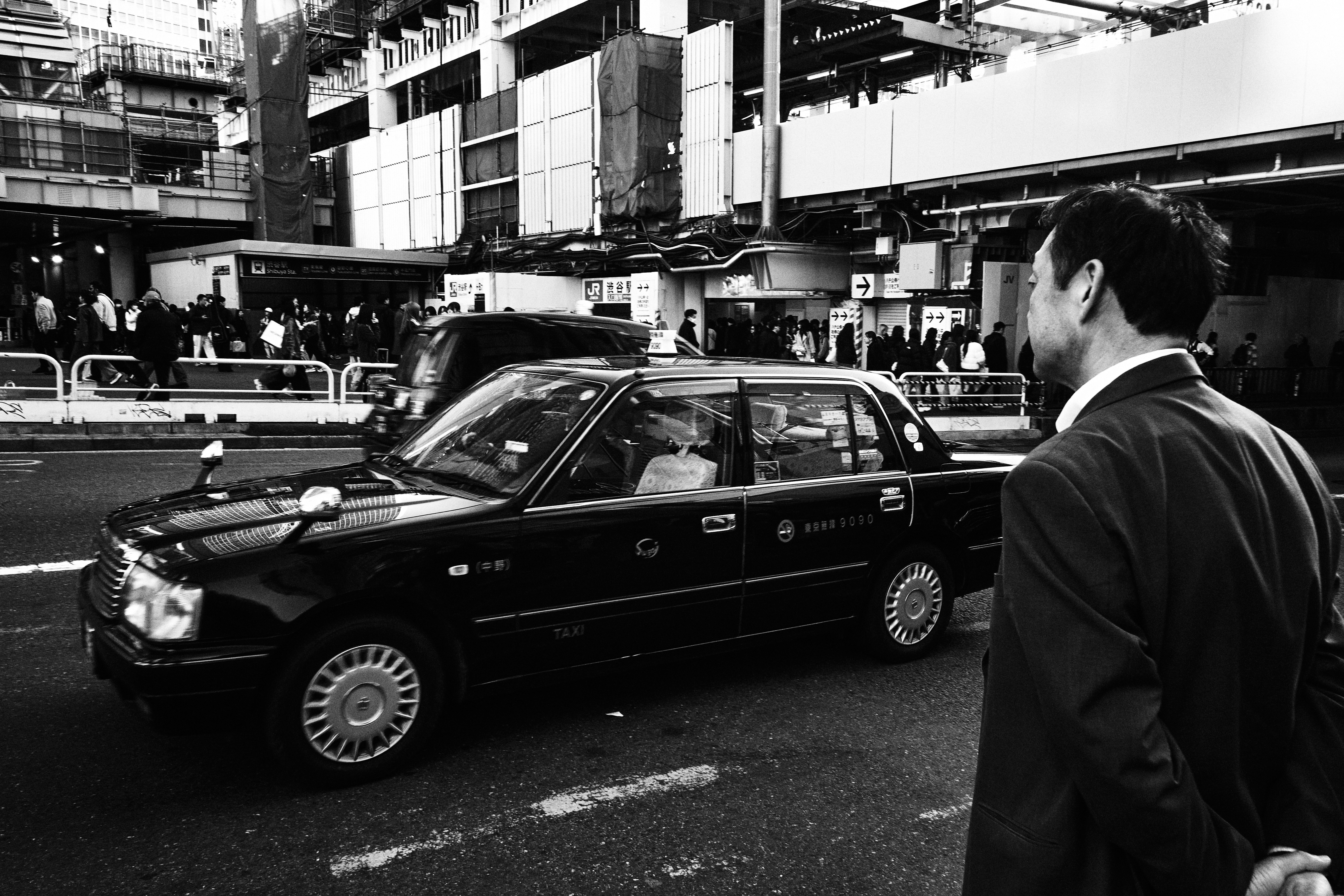 Man in suit waits for black taxi on city street.