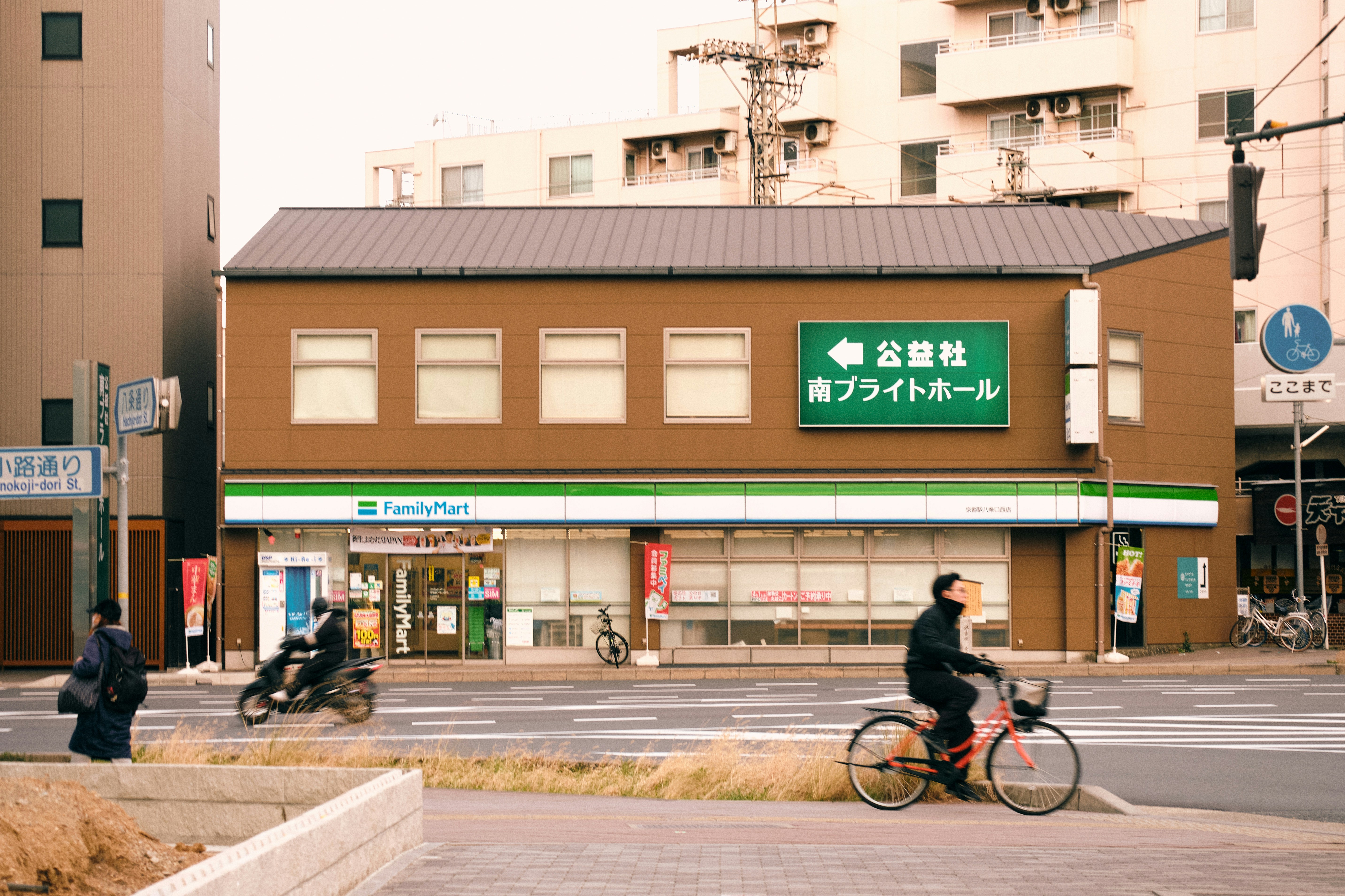 A brown convenience store with people on bikes and scooters.