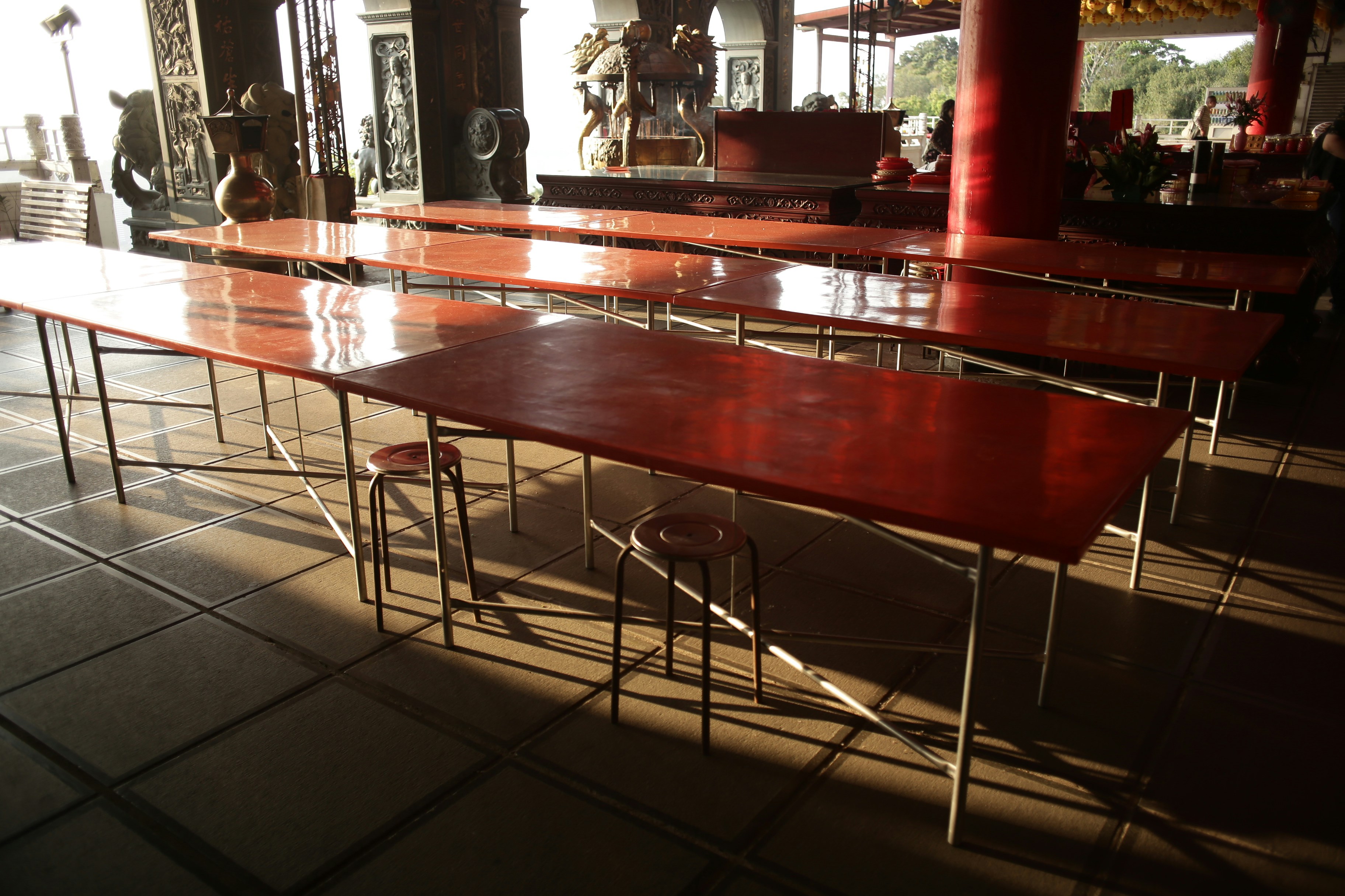 Mesas e bancos longos e vermelhos em um quarto iluminado pelo sol.