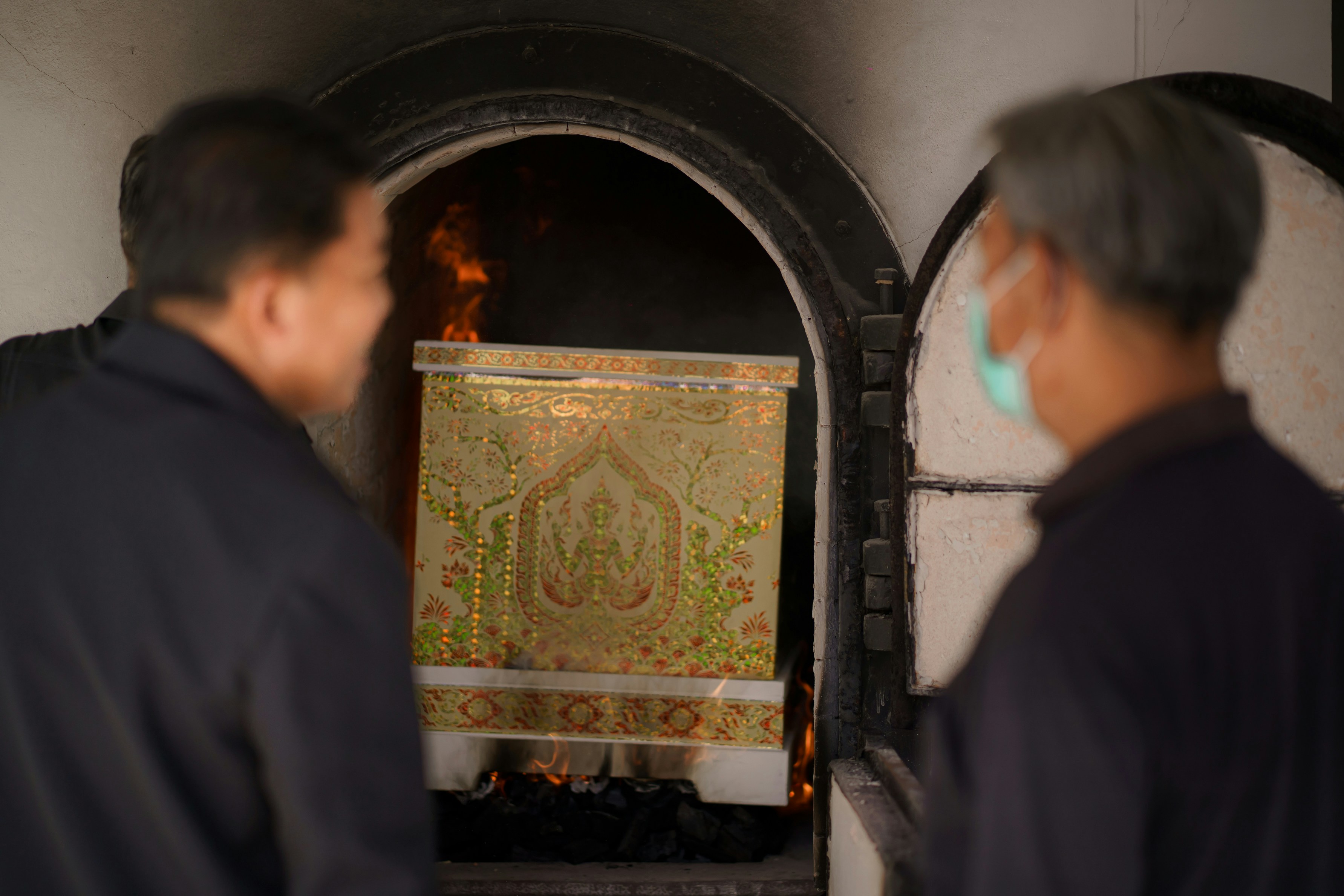 Two men watch a coffin being cremated in a furnace.