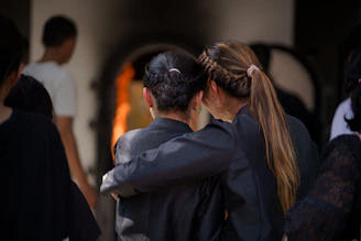 Two women embrace in front of a cremation furnace