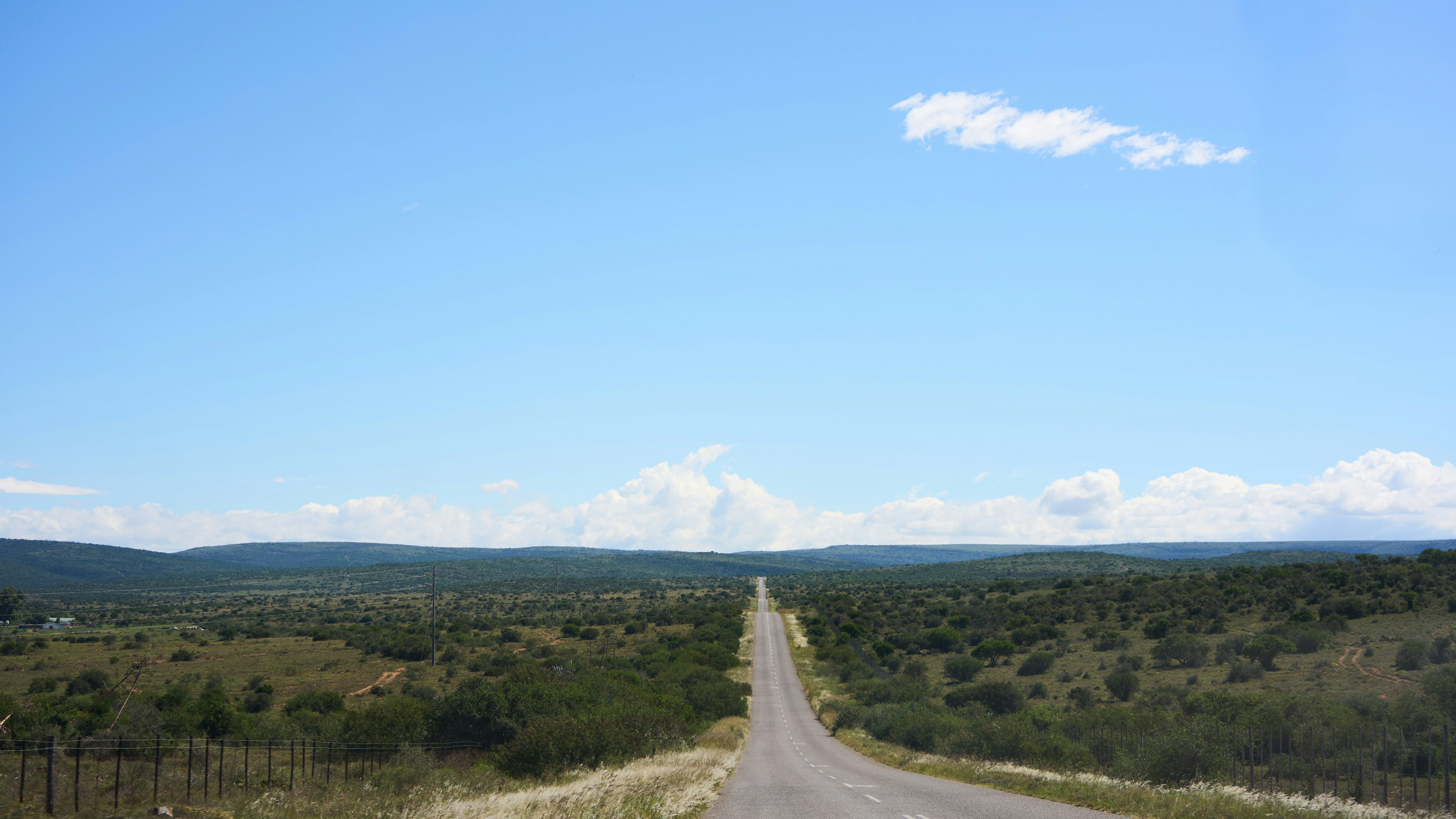 Straight road through a vast green landscape under blue sky.