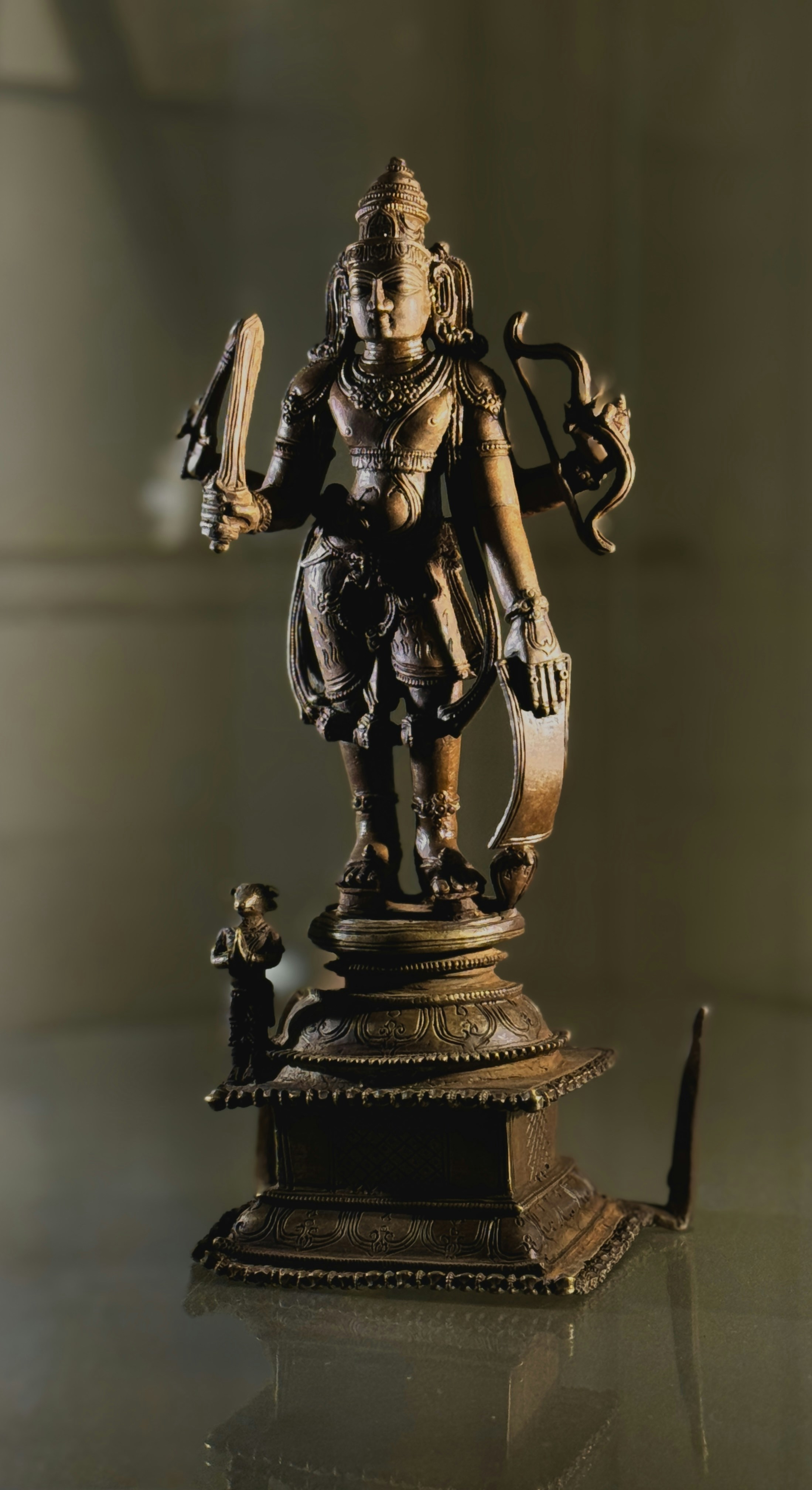 Estátua de bronze de uma divindade segurando uma espada e um arco.