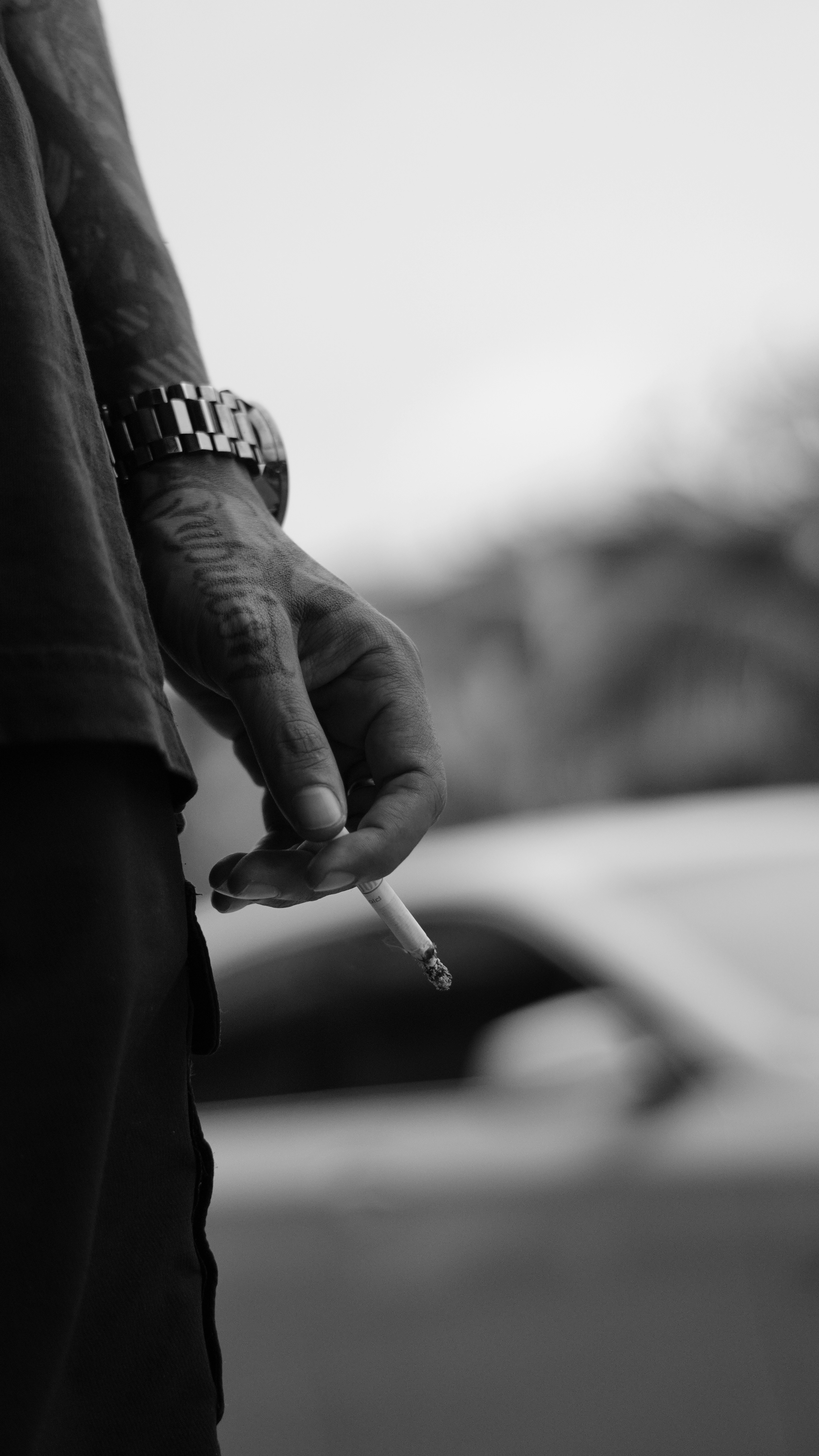 Man holding a lit cigarette with a watch.