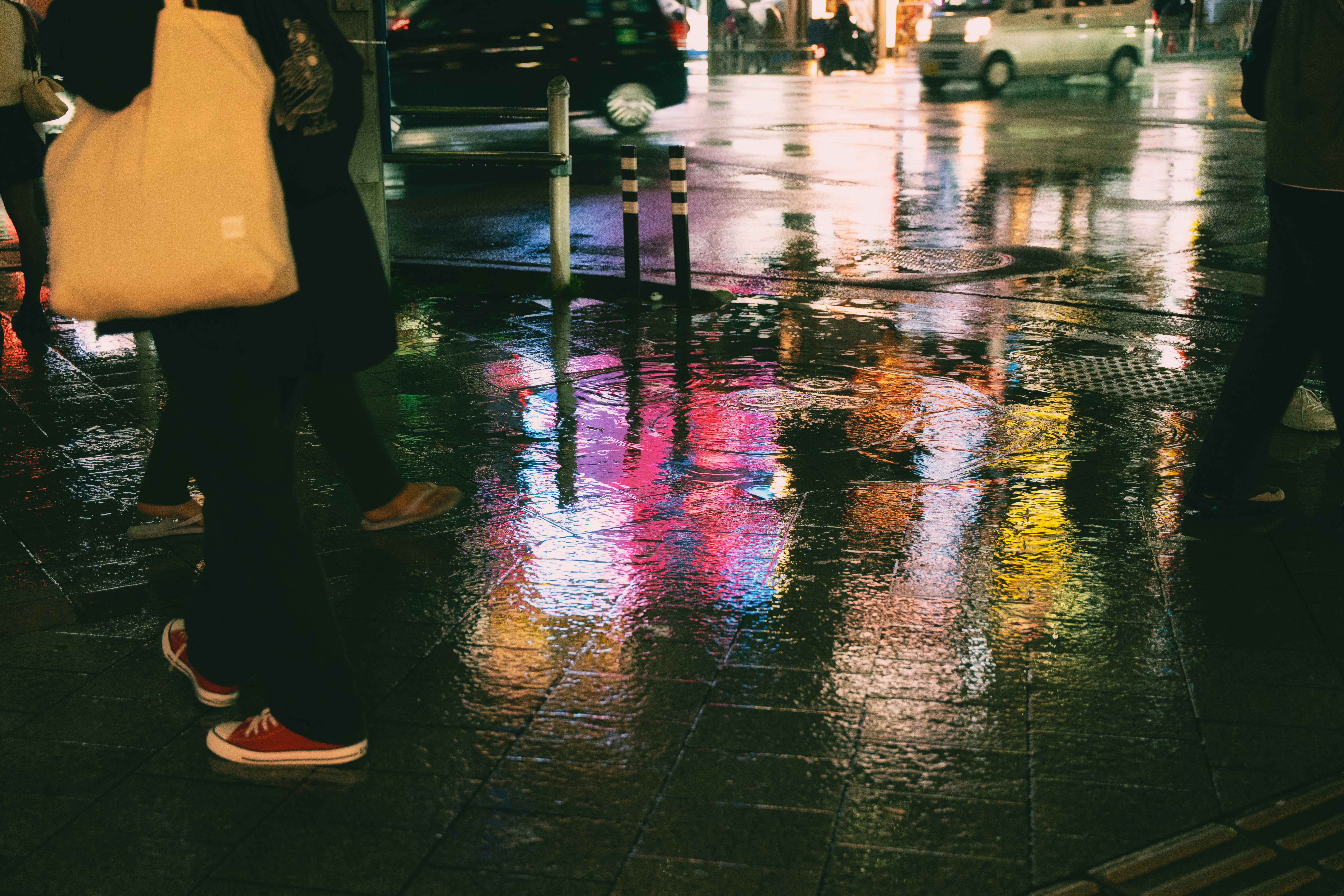 ネオンの反射に映る濡れた街の通りを歩く人々。