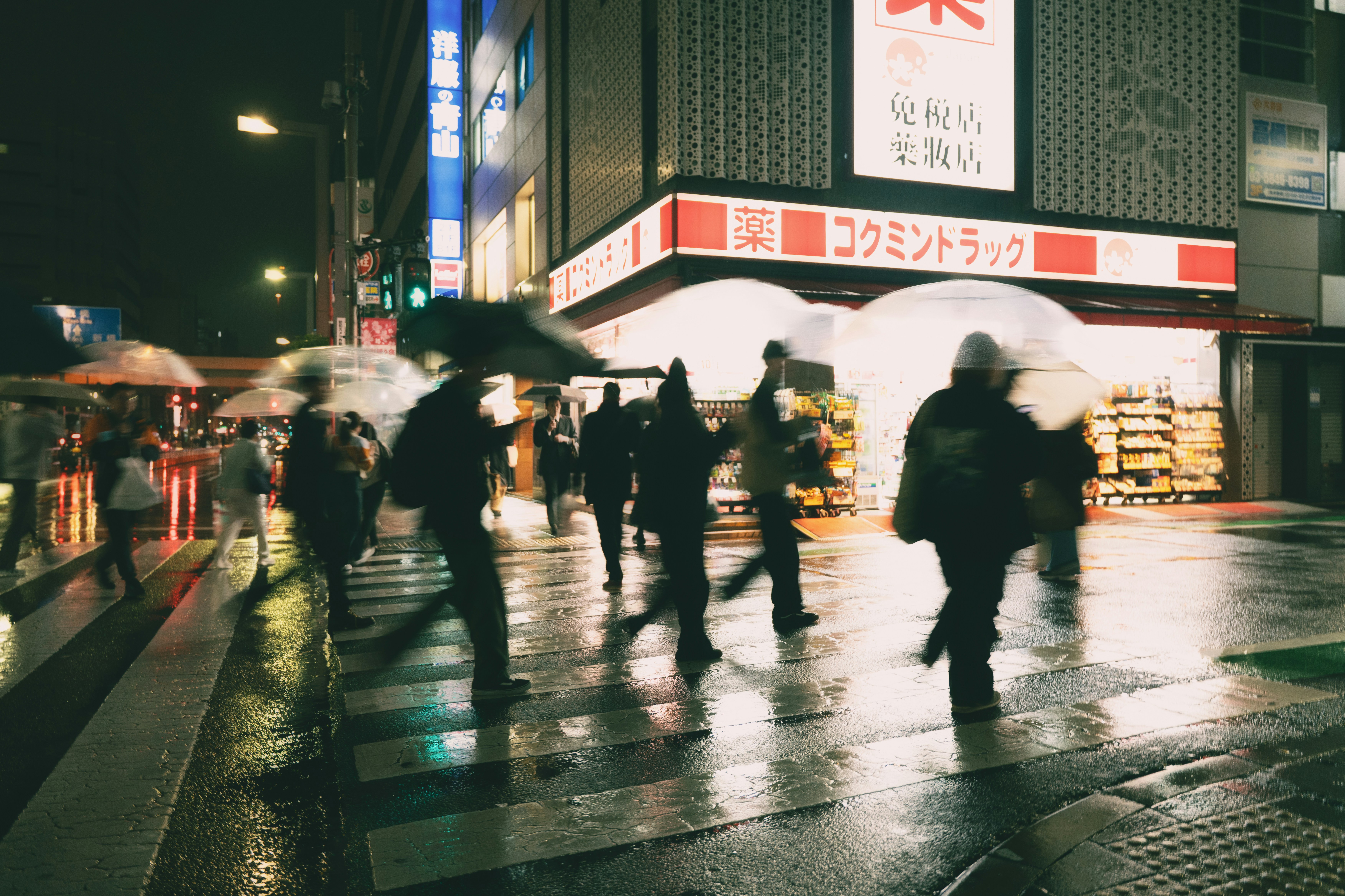 People with umbrellas cross a wet street at night.