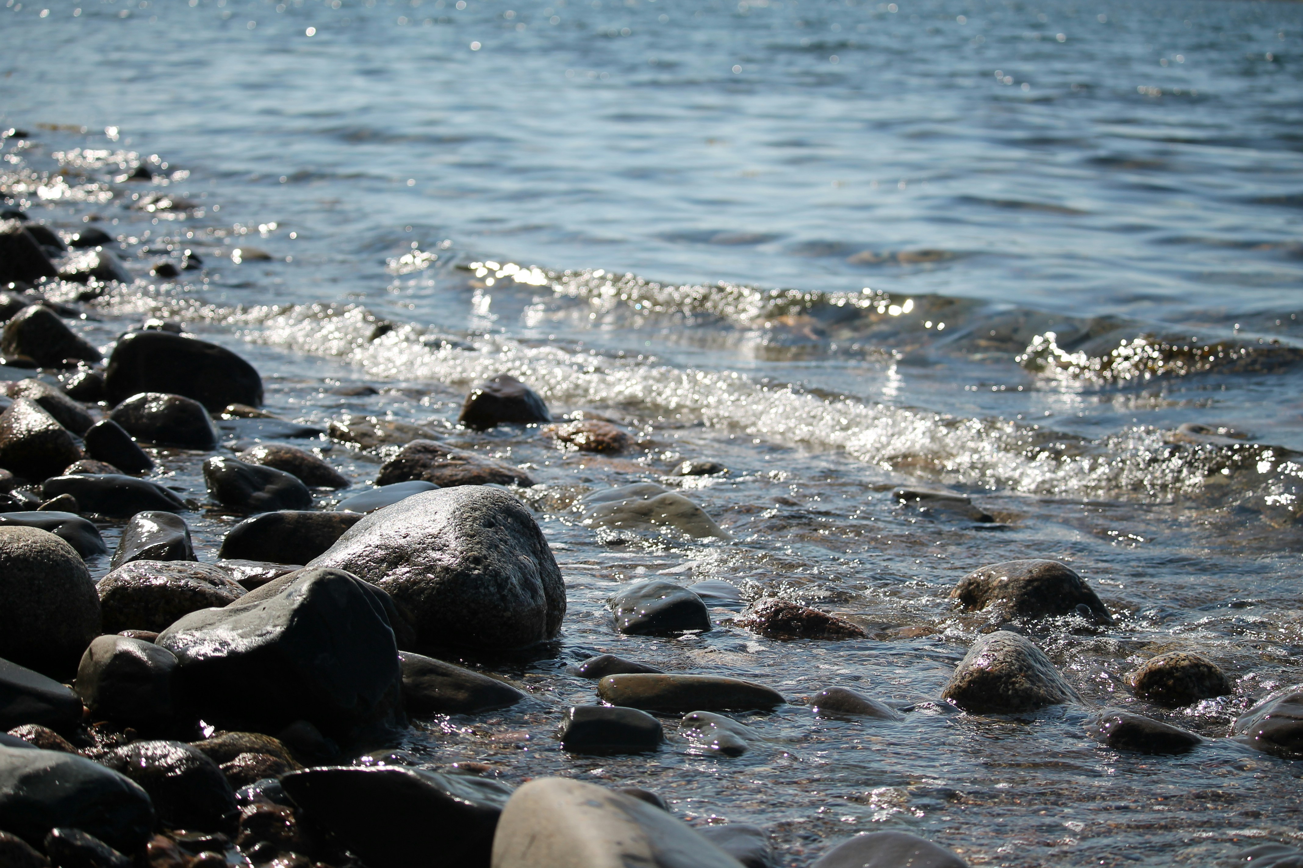 Waves gently lap a rocky shore under sunlight.