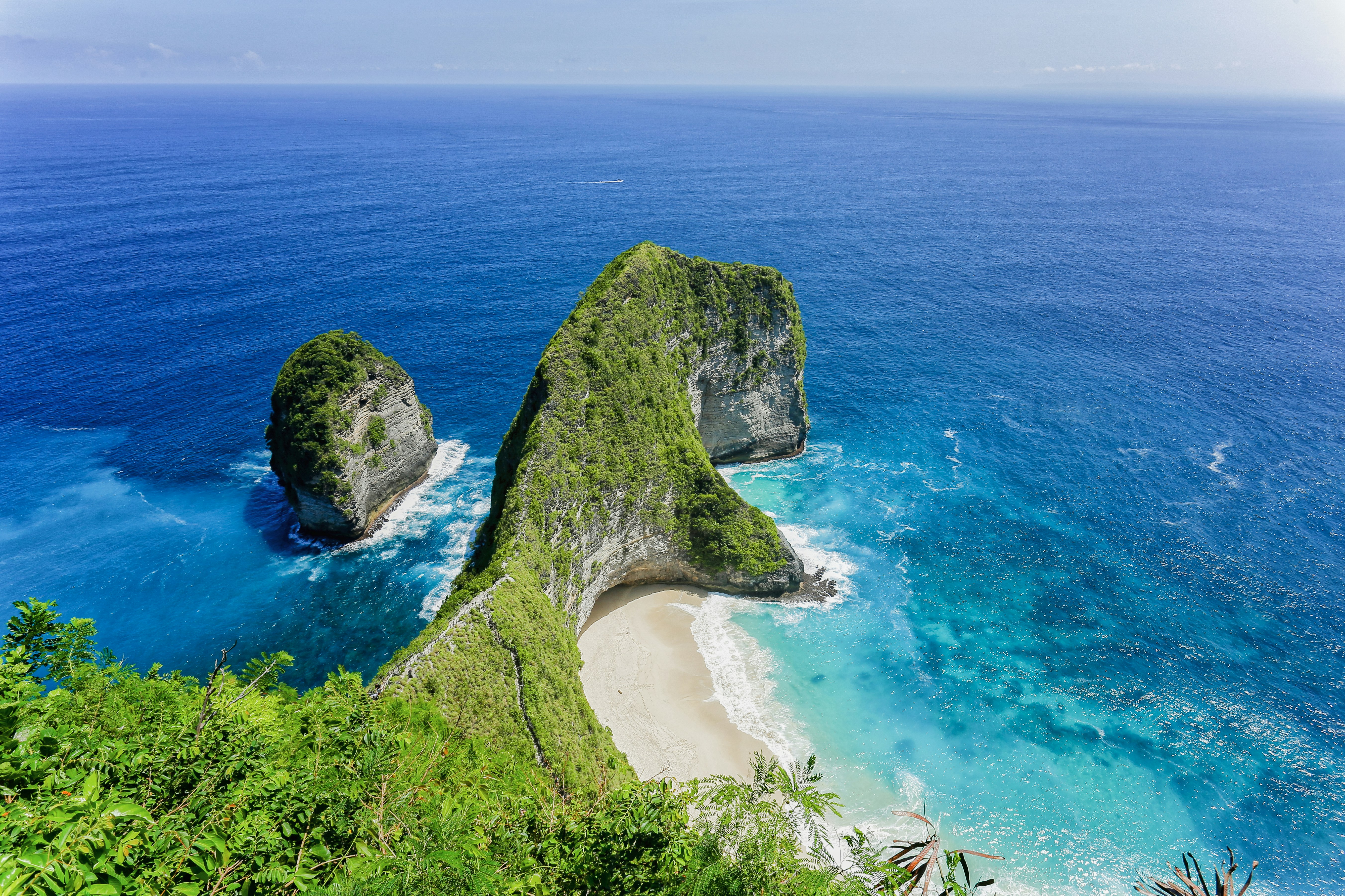 Grüne Klippen überblicken einen tropischen Strand und ein türkisfarbenes Meer.