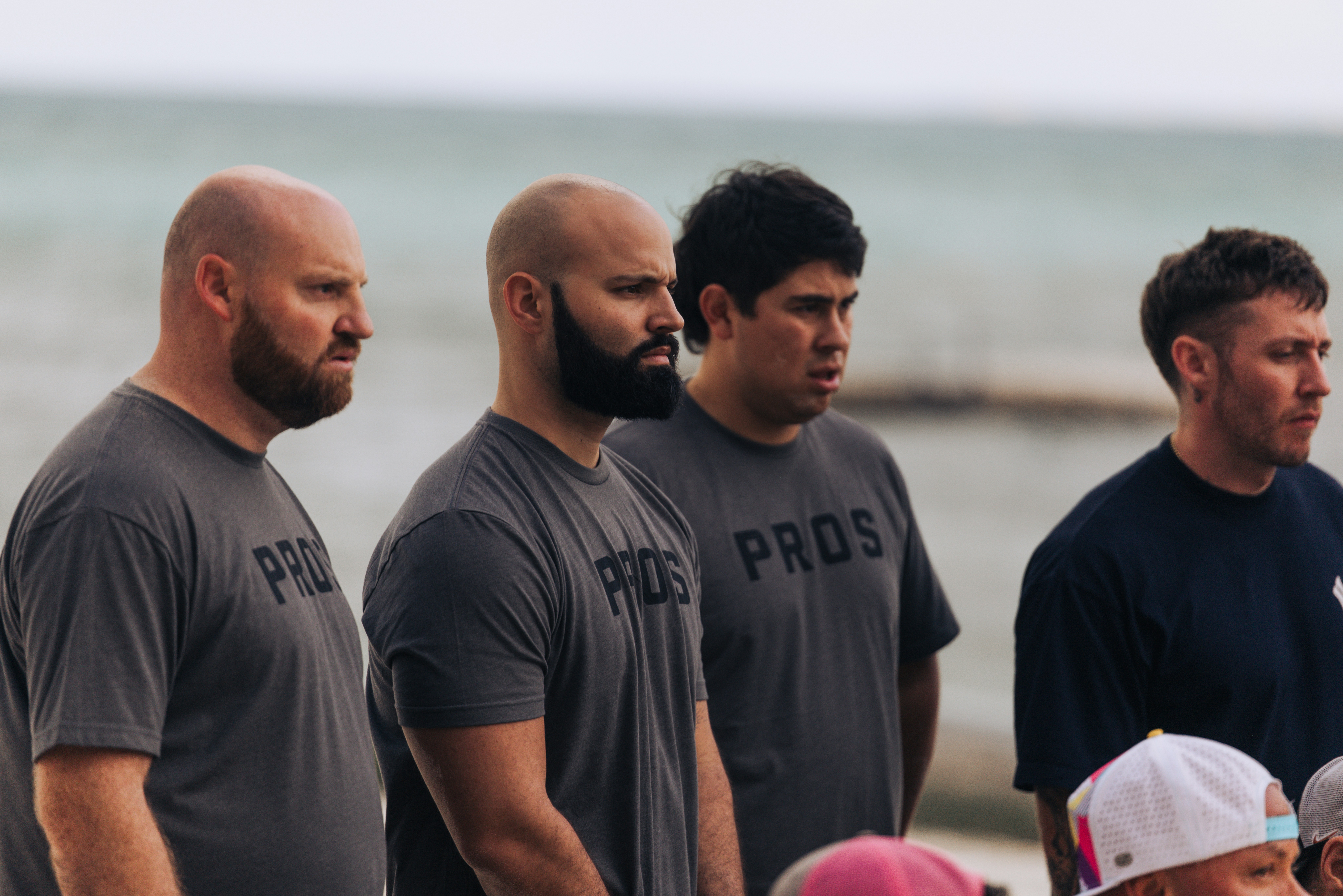 Four men in grey t-shirts stand looking forward.