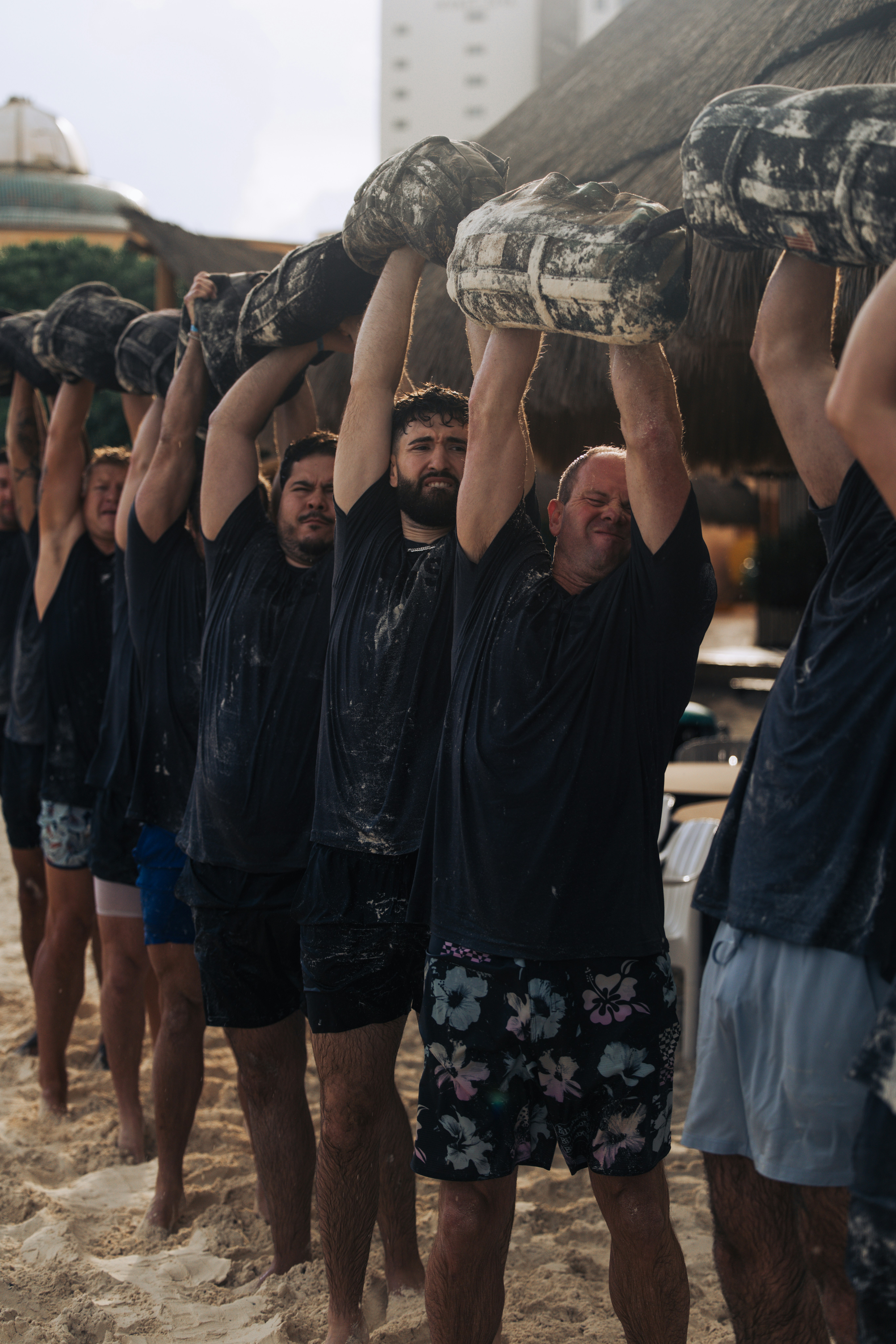Men carrying heavy logs on a sandy beach