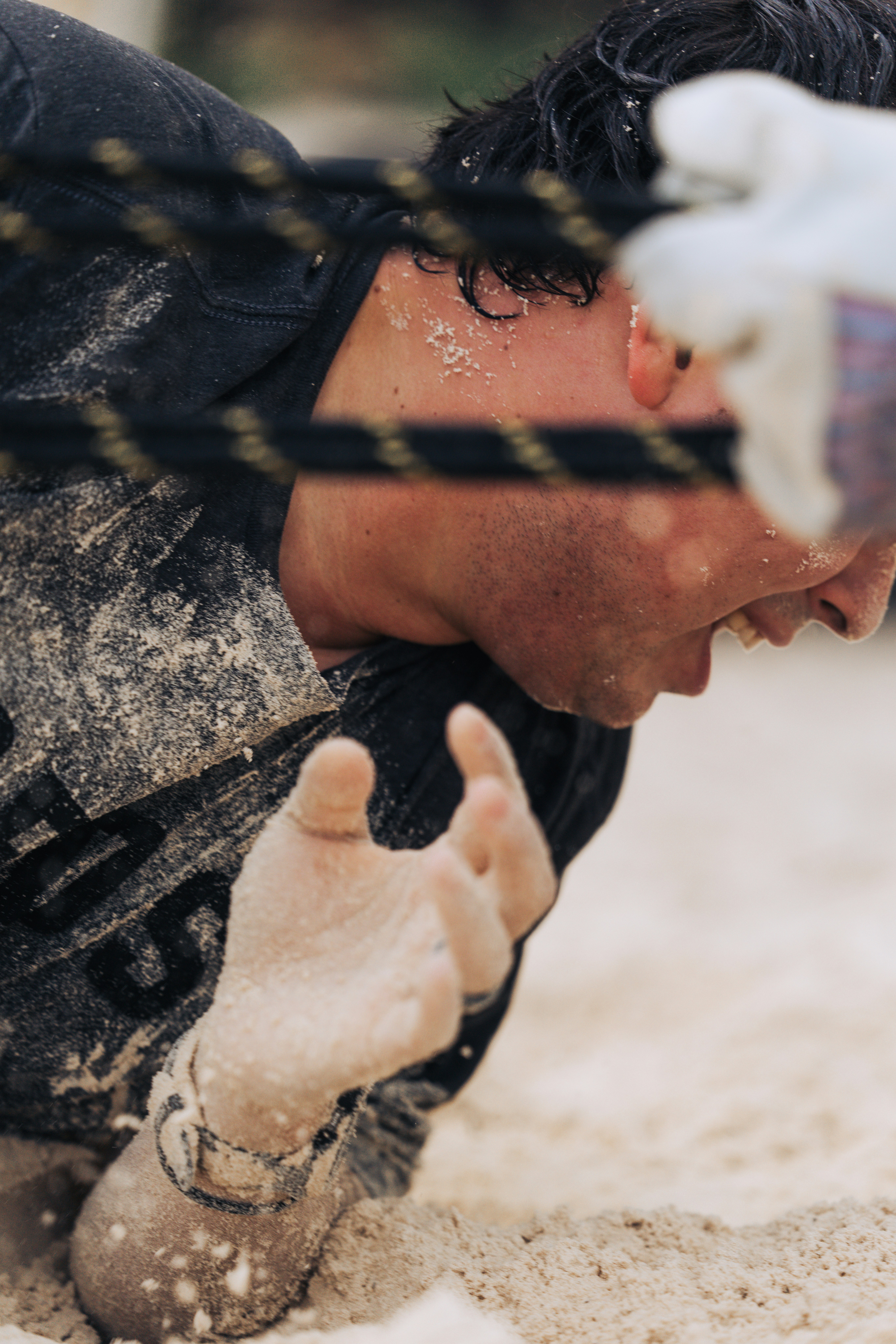 A man struggling in the sand with a rope