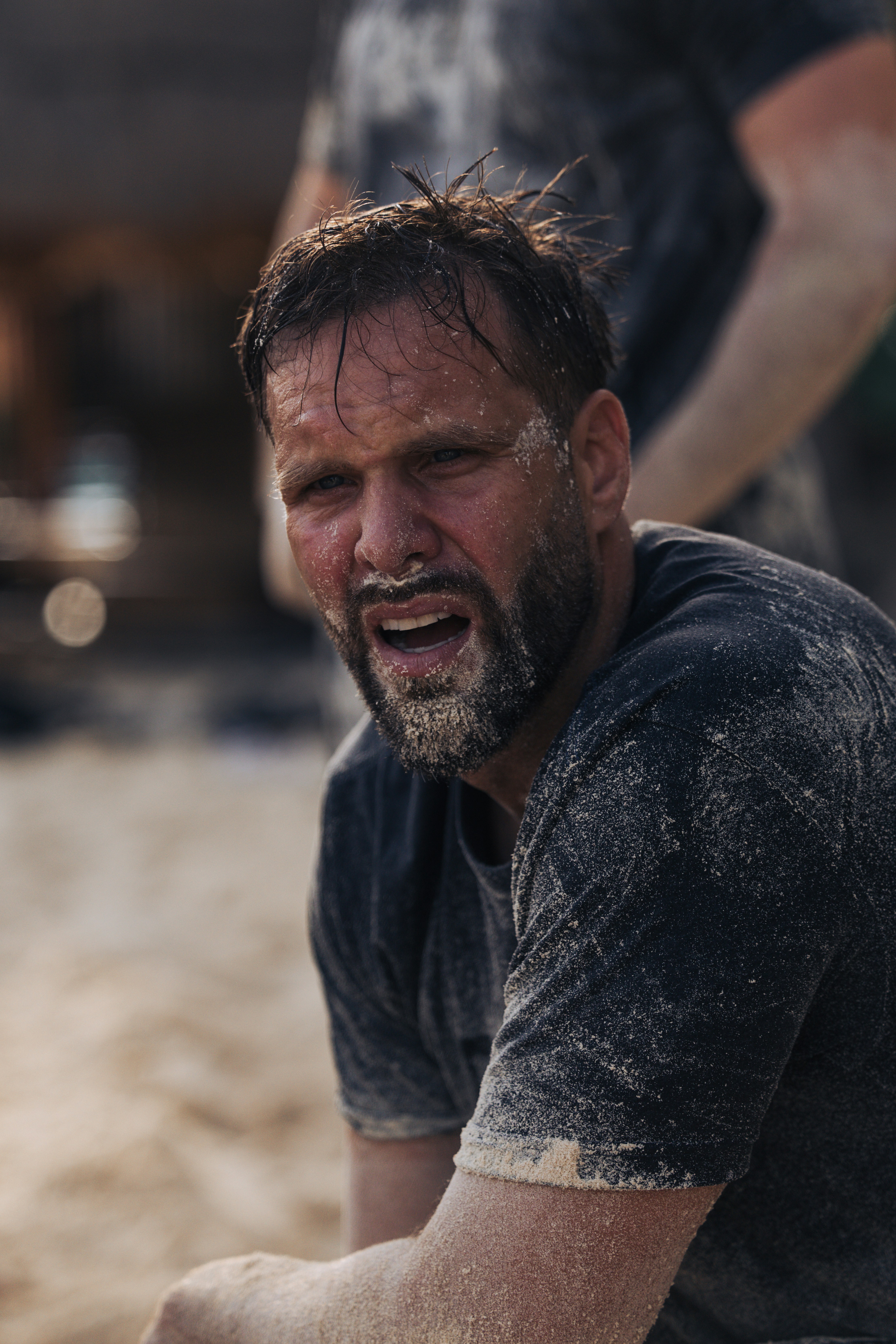 Man covered in sand, looking tired and strained