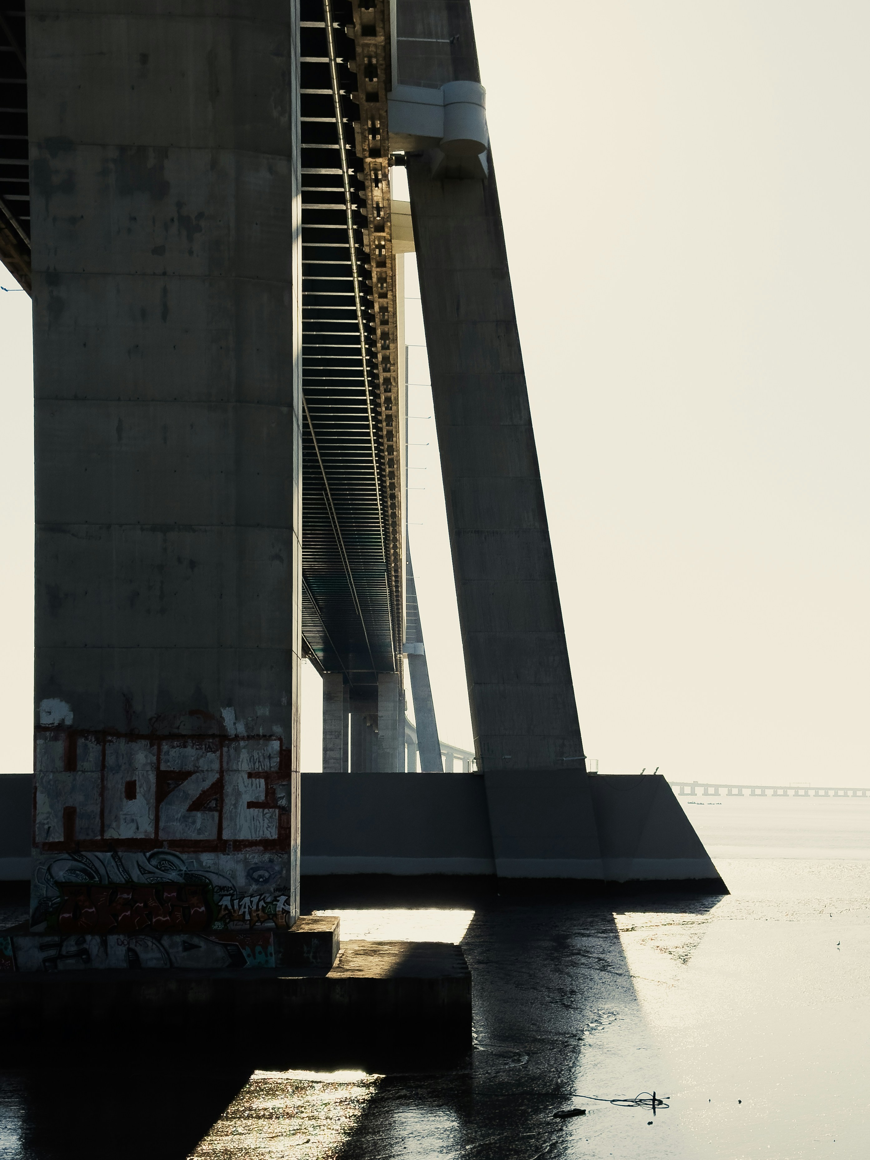 Concrete bridge supports over calm water with graffiti.