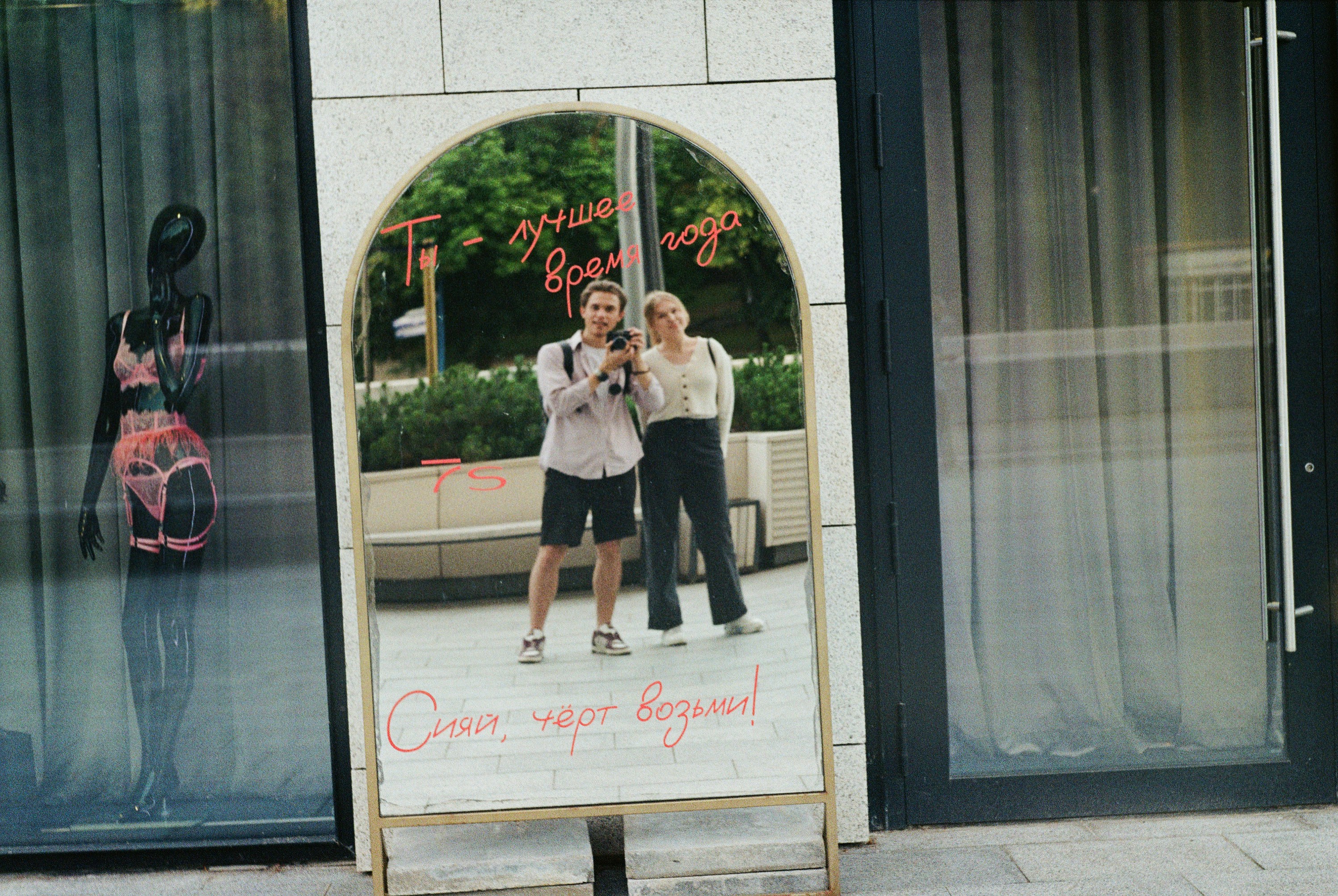 Two people taking a mirror selfie outside a store.