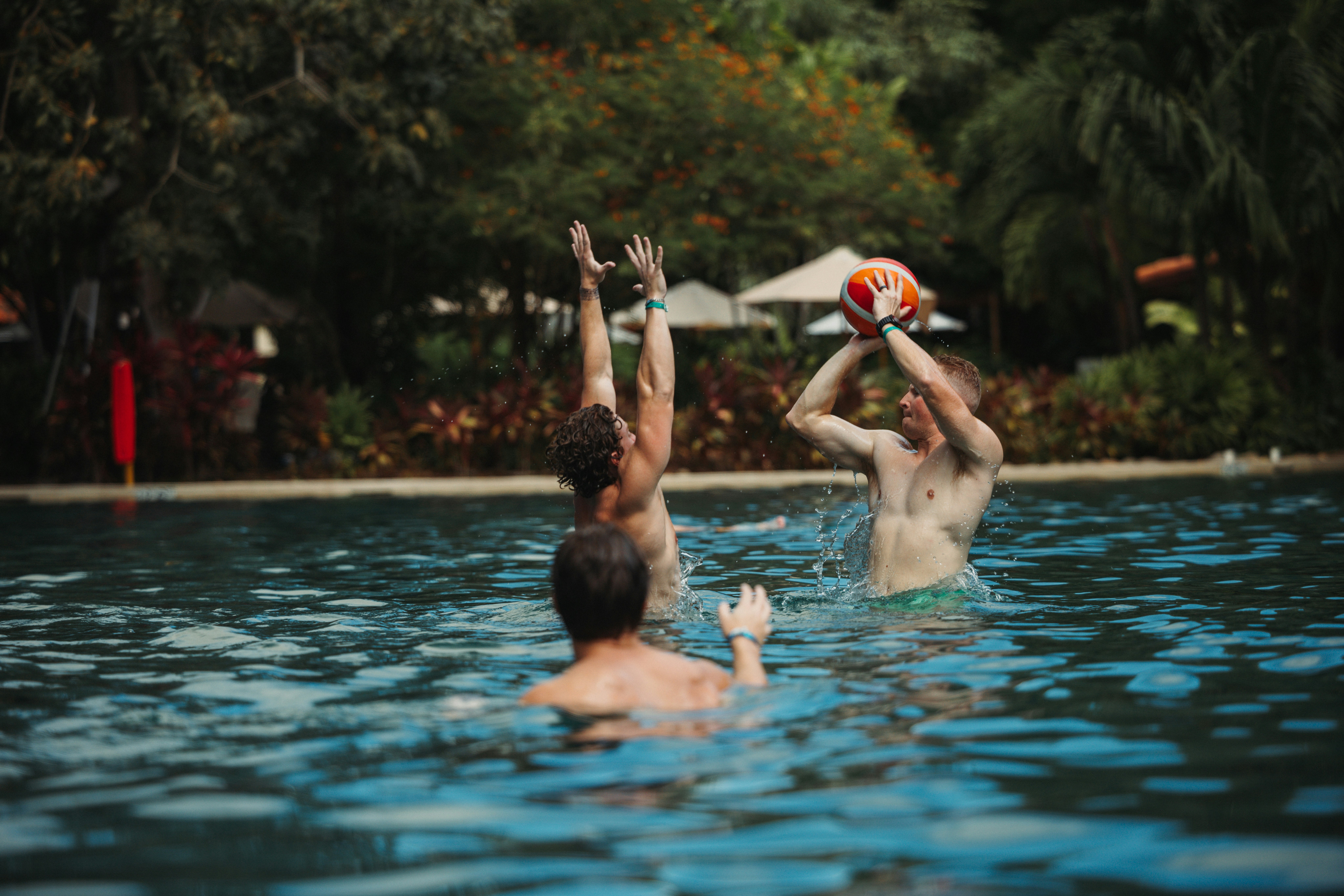 Tiga pria bermain bola voli di kolam renang