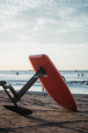 Orange surfboard with foil on sandy beach