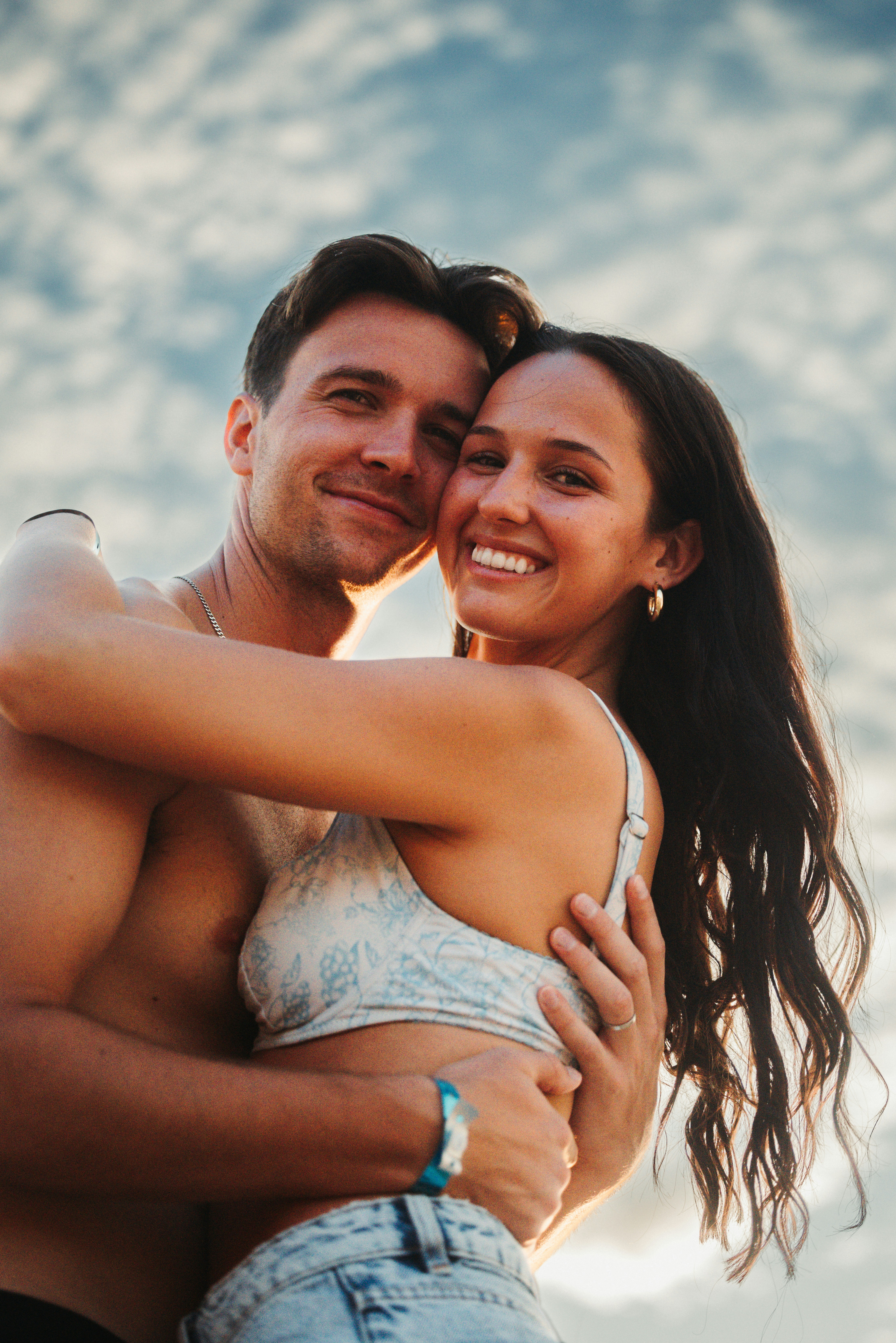 Um casal se abraça em uma praia ao pôr do sol.