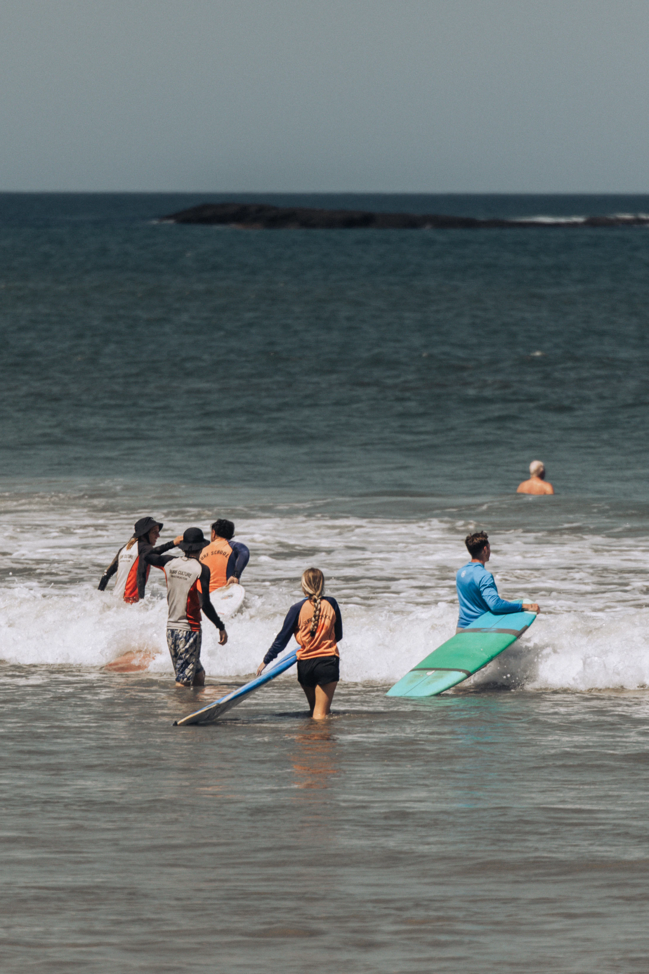 Surf instructor and learners entering the water with different surfboards