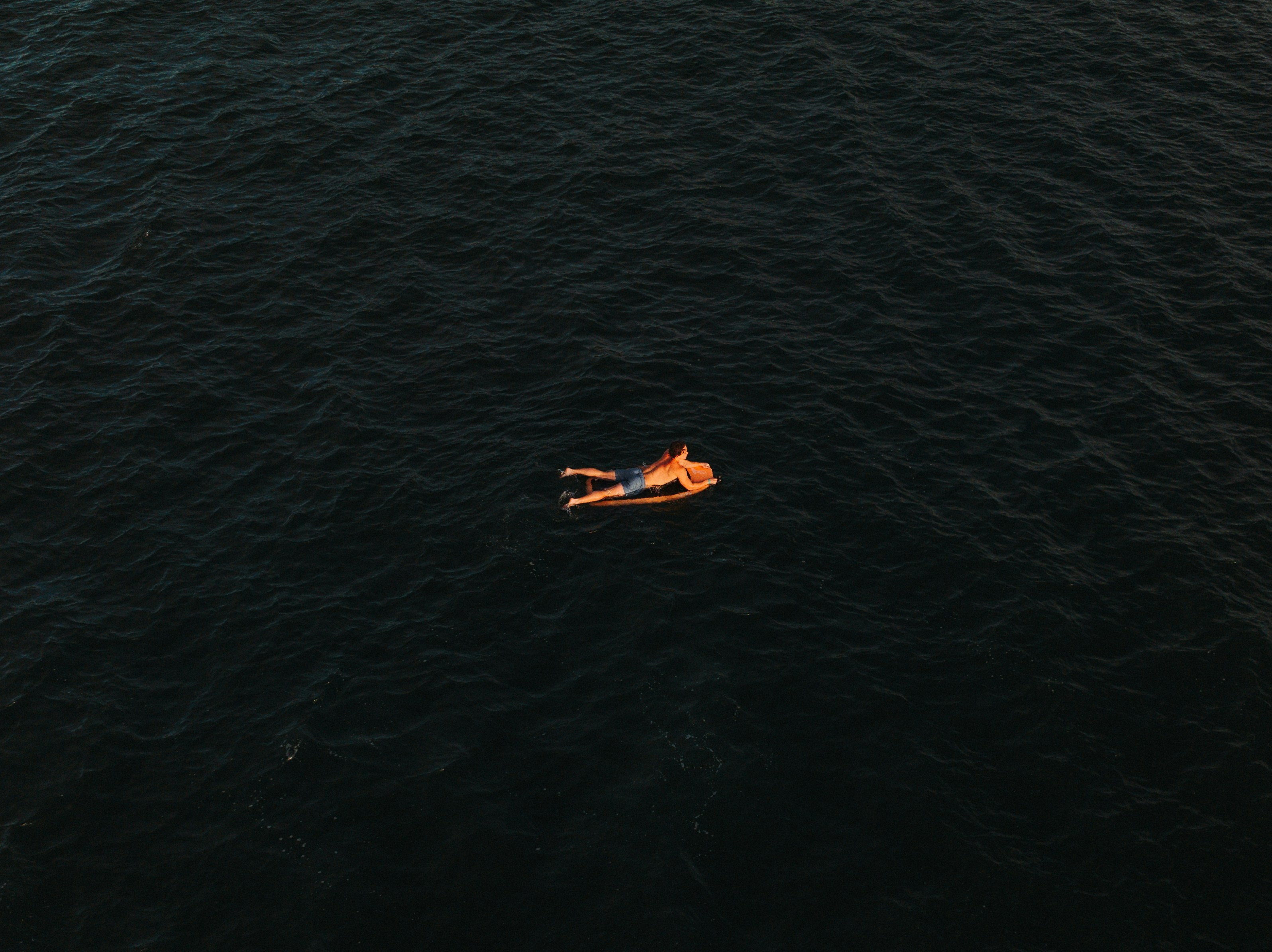 Person floats on inflatable raft in dark ocean.