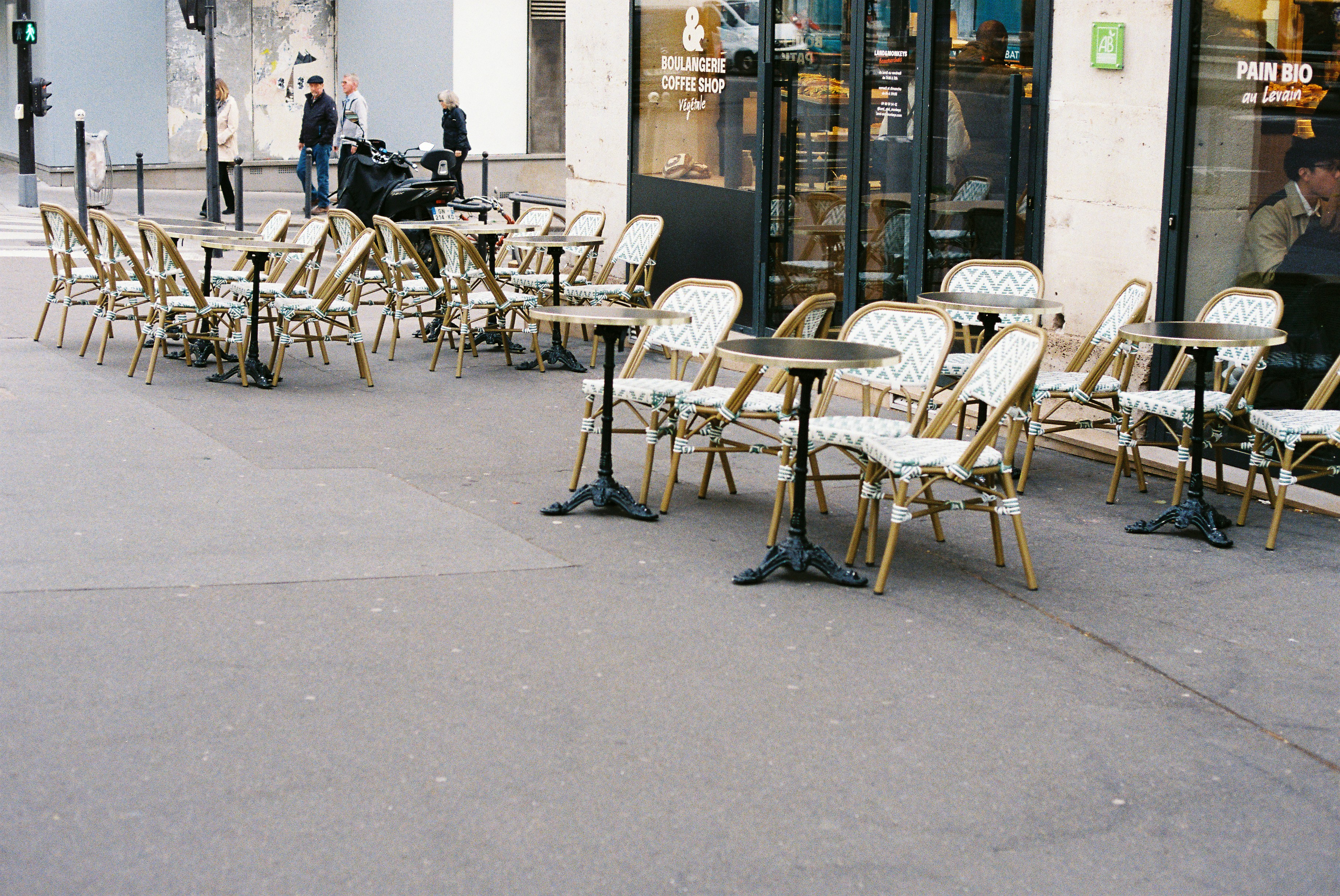 Empty outdoor cafe tables and chairs on a sidewalk.