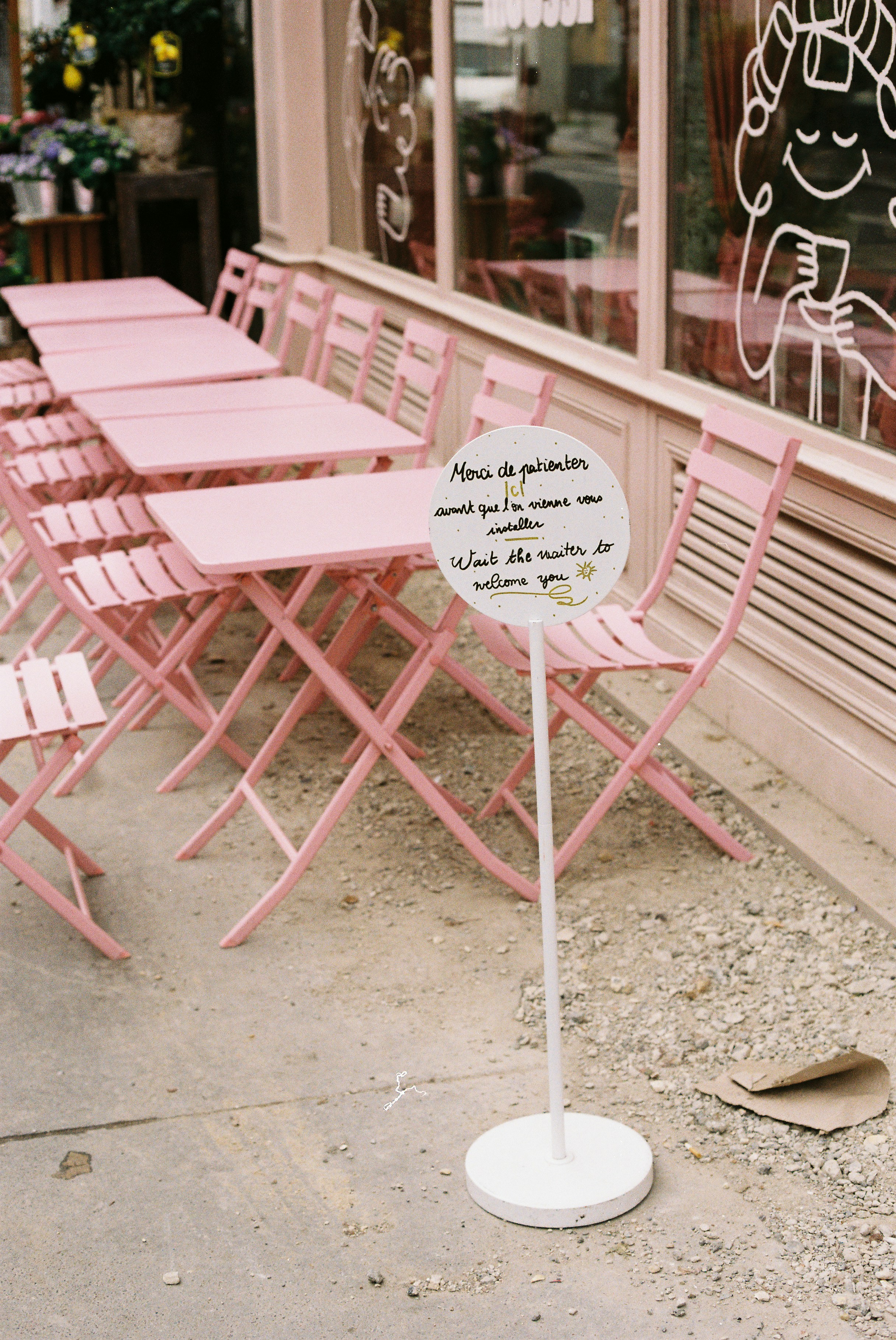 Mesas y sillas rosas al aire libre de café cubren una acera.
