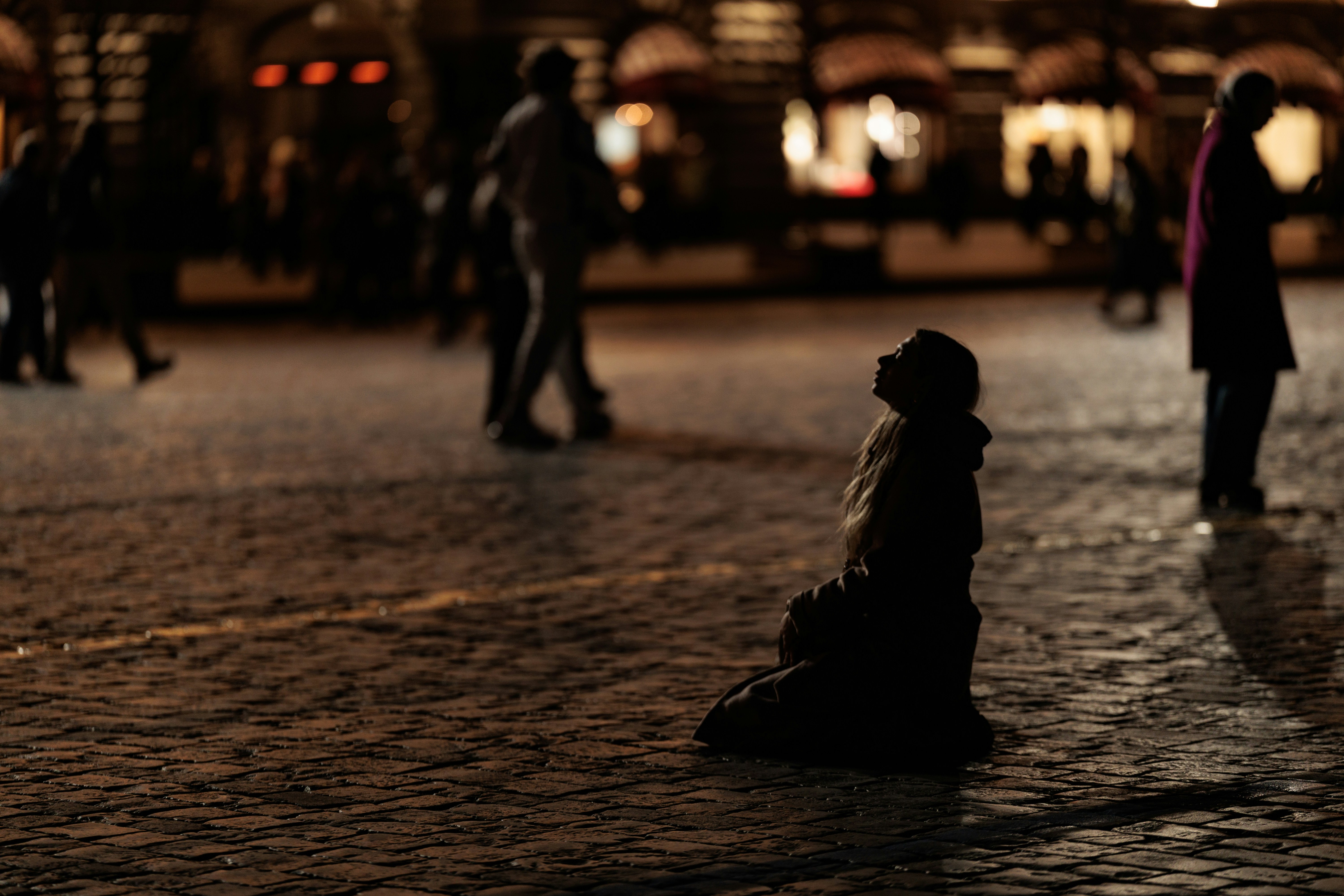Silhouette einer Person, die nachts auf Kopfsteinpflaster kniet.