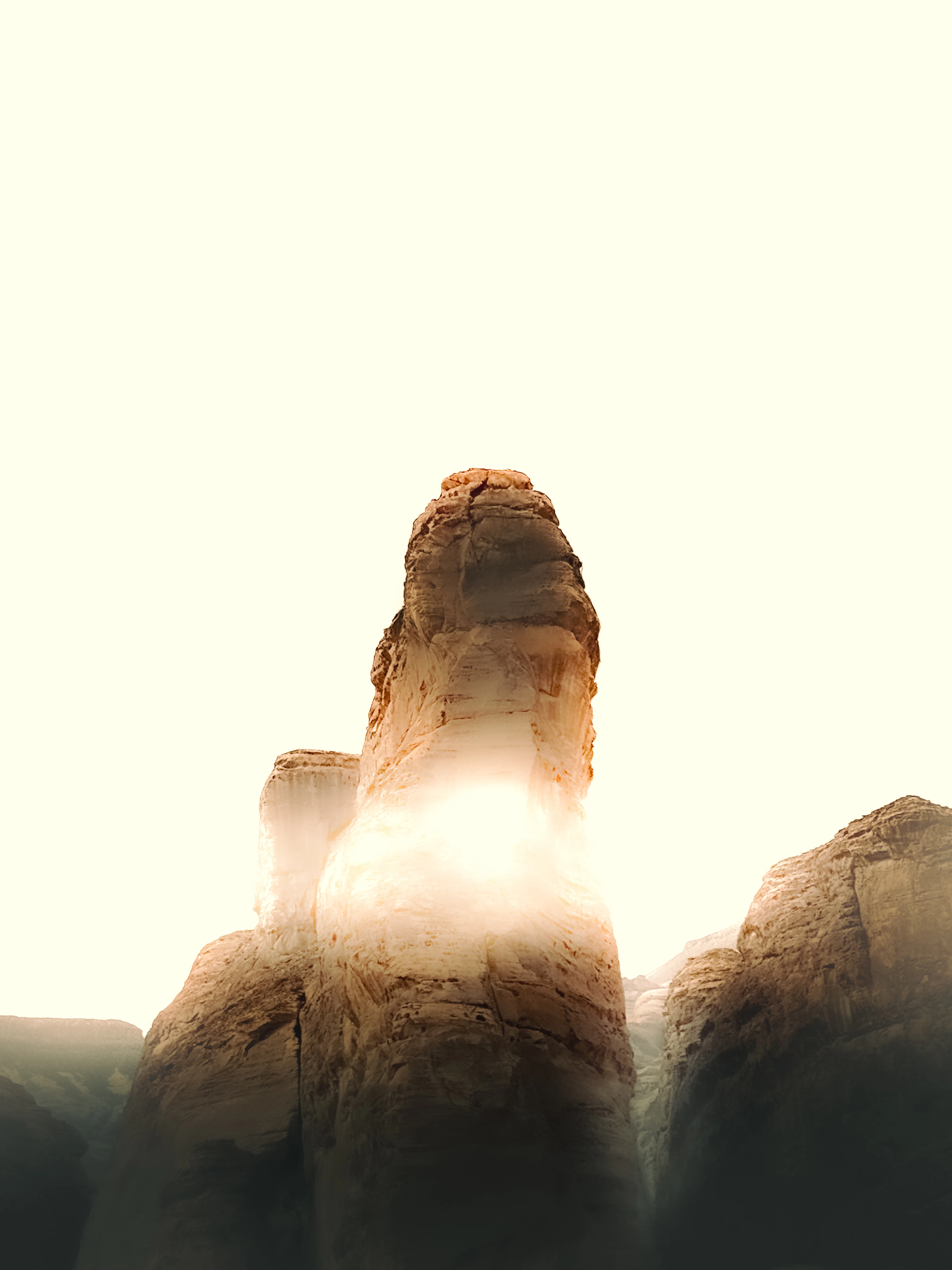 A towering sandstone rock spire backlit by hazy golden sunlight against a pale sky.