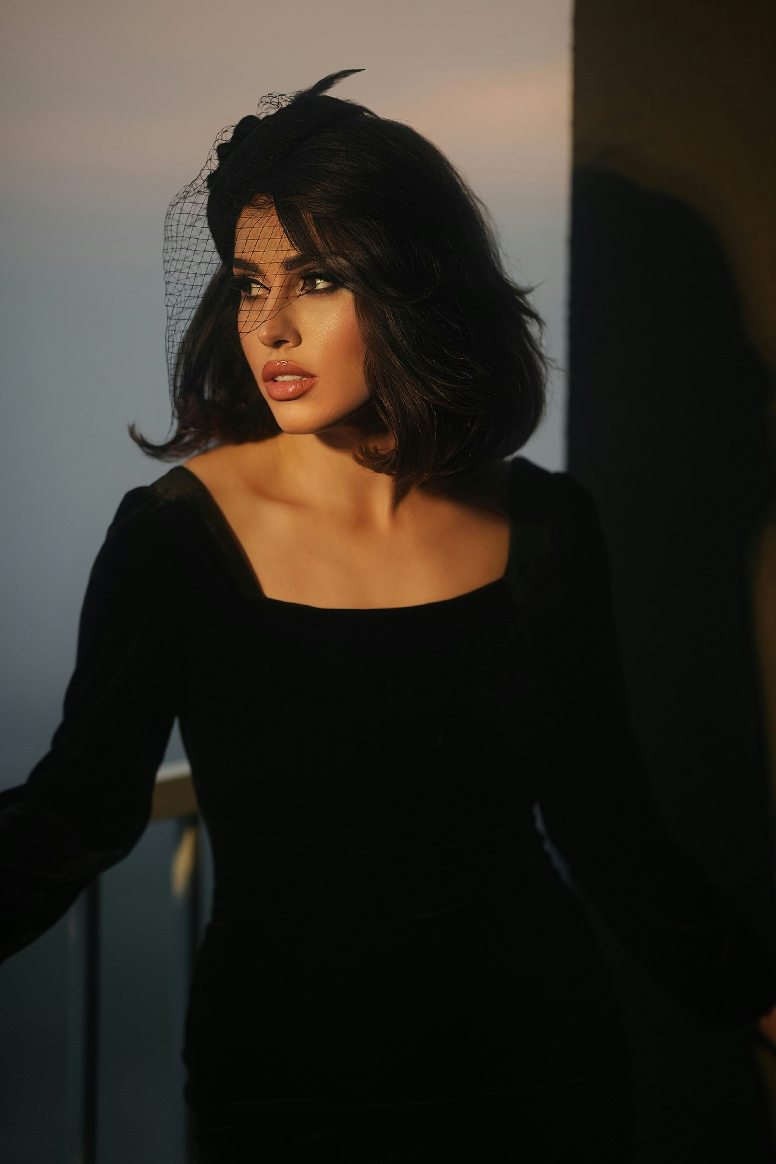 Companion in a black dress and sheer veil, gaze lowered