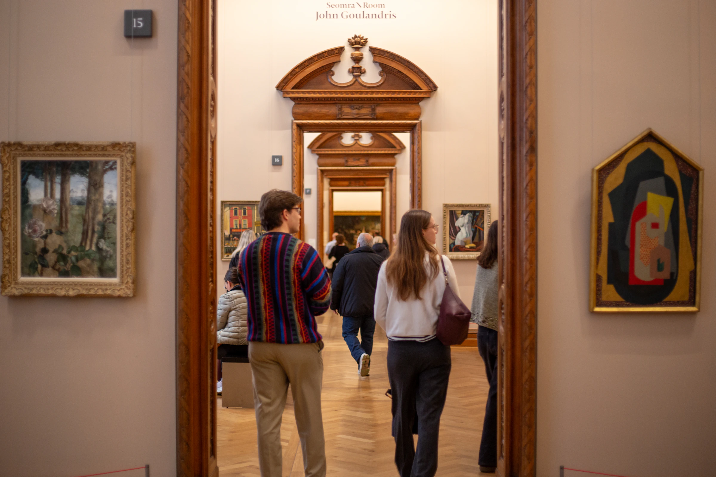 Visitors moving through a museum gallery lined with paintings