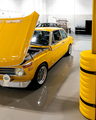 A bright yellow vintage car with its hood open